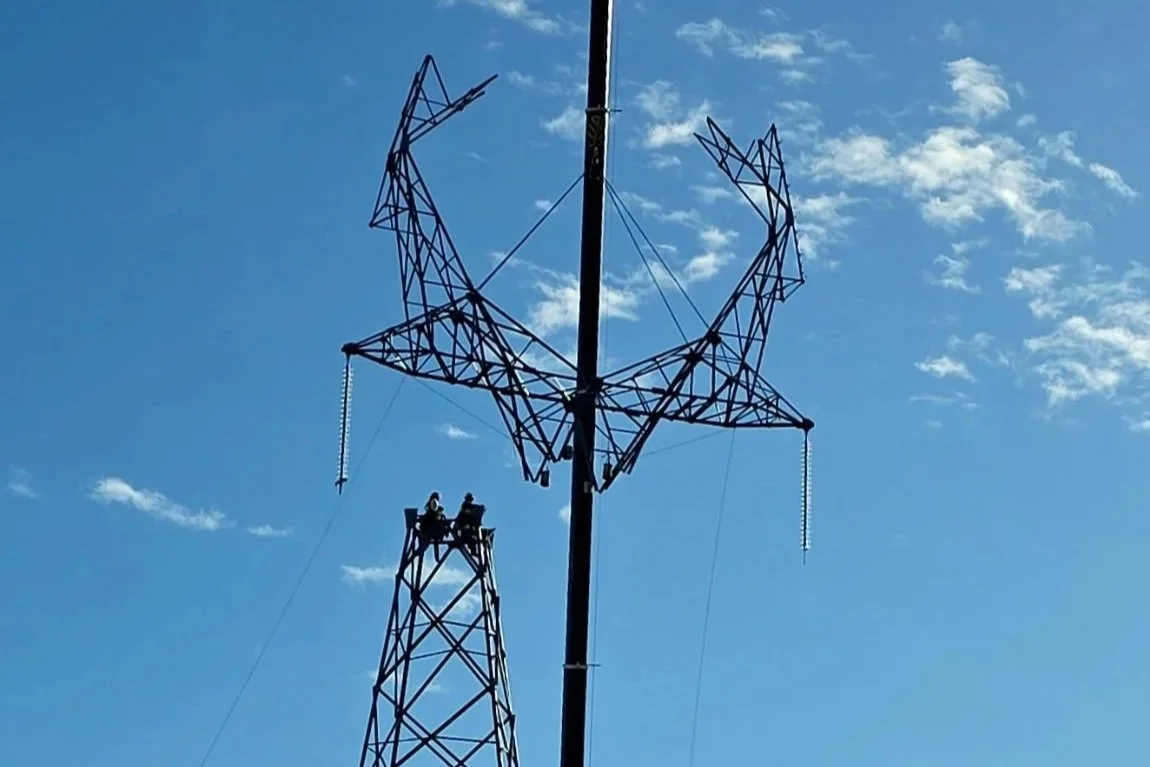 A metal antenna tower with a star-shaped sculpture on top, against a blue sky with scattered clouds.