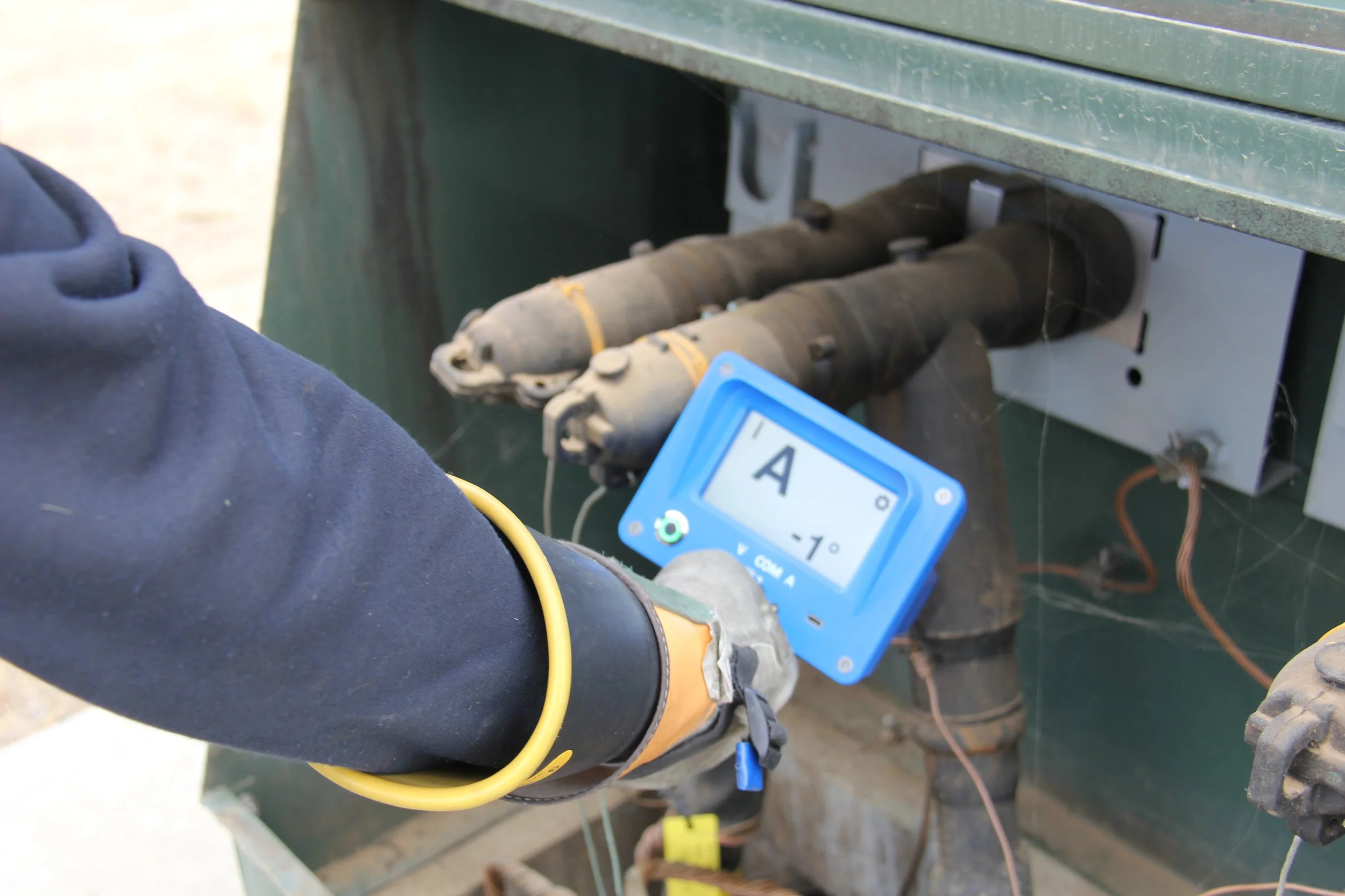 Person adjusting a digital temperature gauge on electrical wiring inside a green metal box, with wires and fixtures visible.