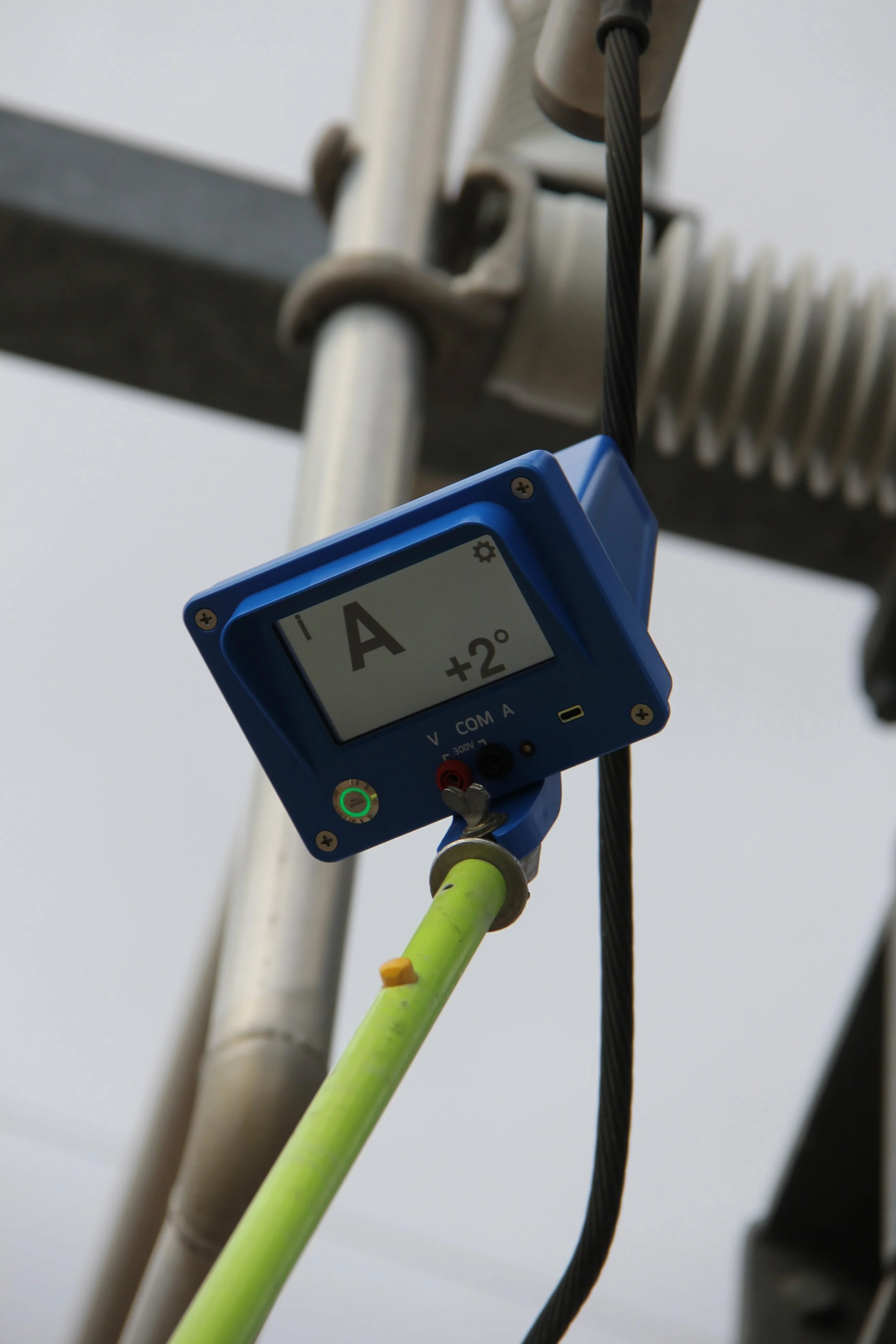 A digital angle finder displaying +2°, attached to a yellow pipe, mounted on a metal structure with electrical wires and components.