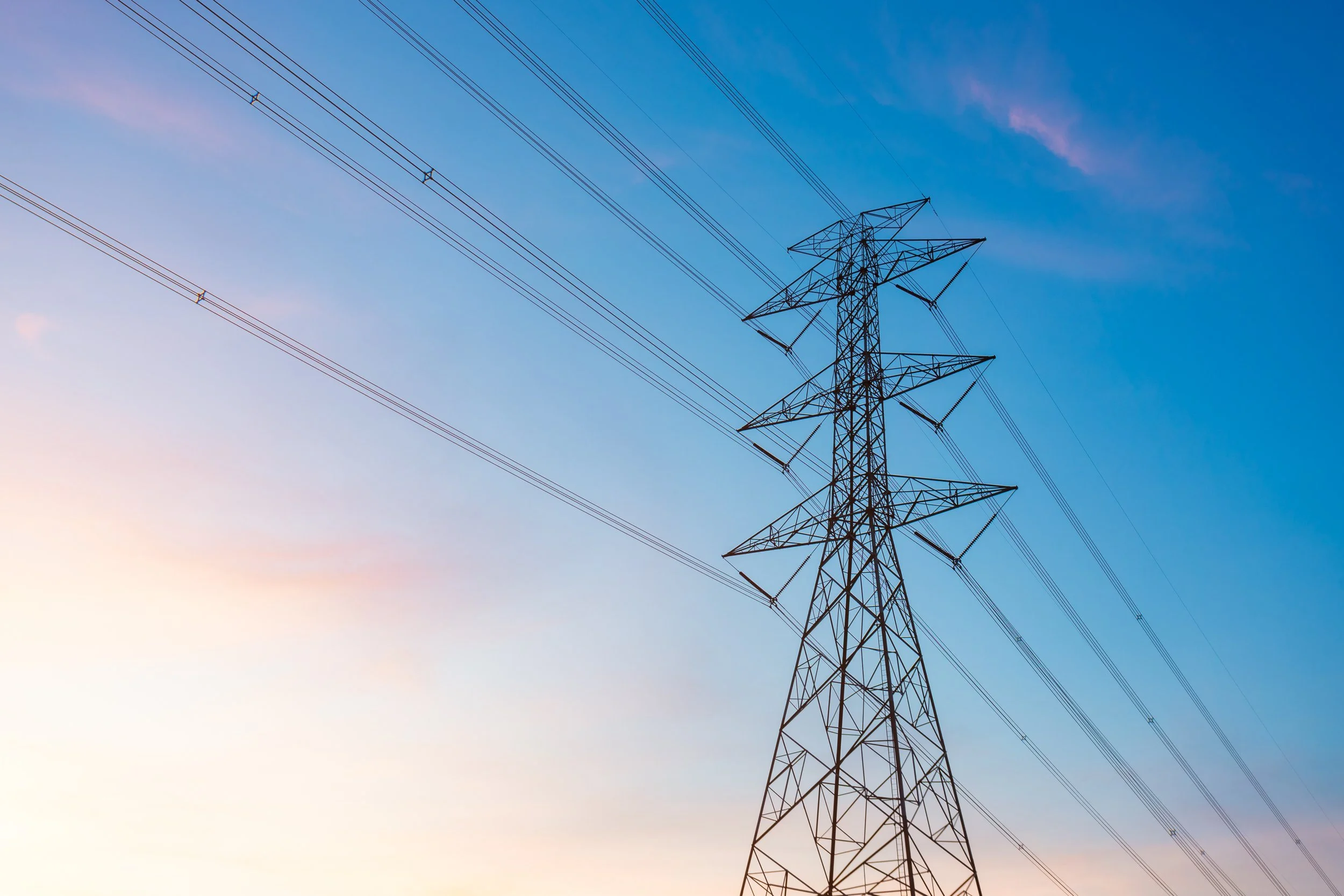 Electric transmission tower with power lines against a blue sky during sunset.