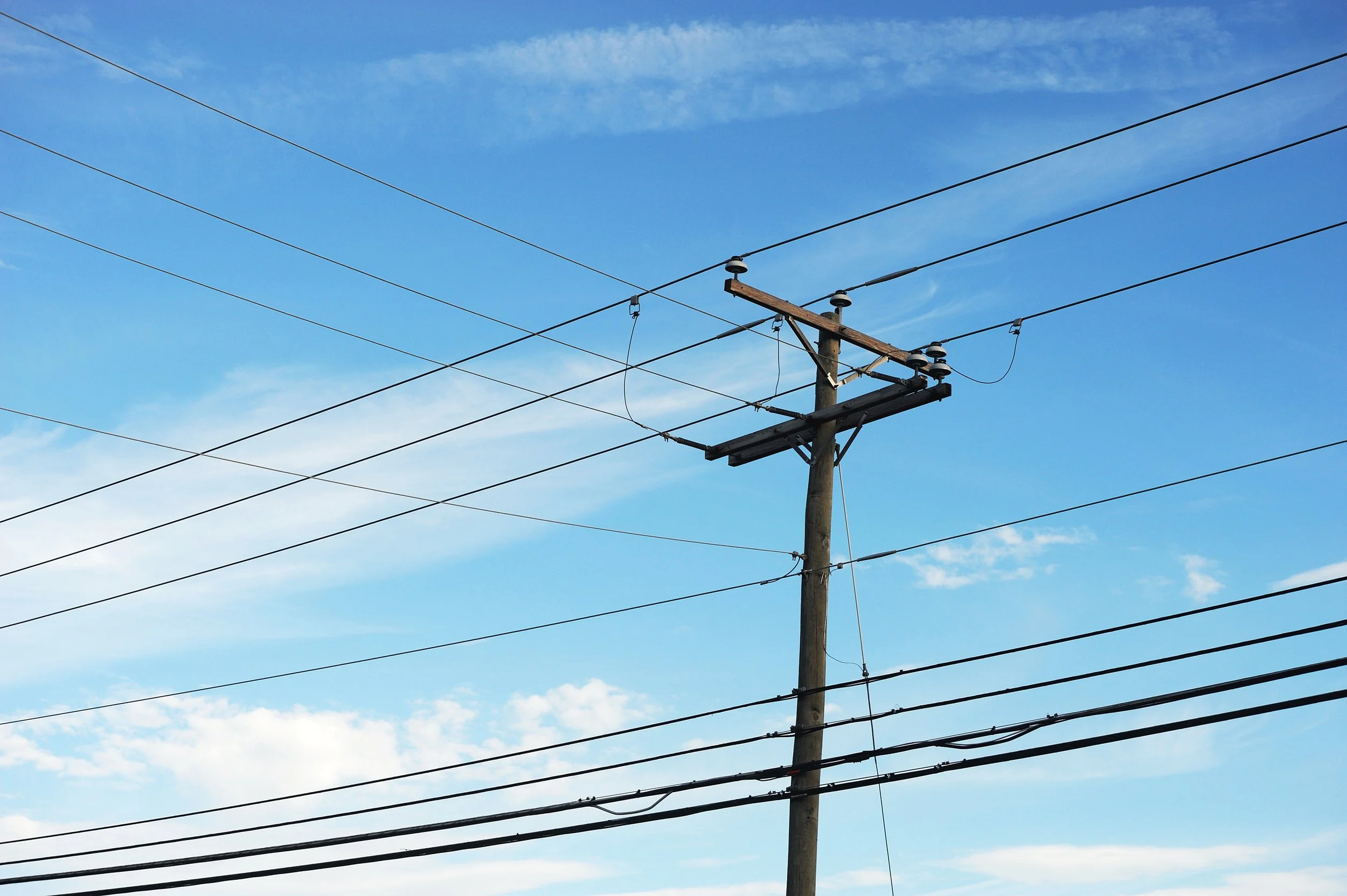 Electric utility pole with multiple power lines against a blue sky with some clouds.