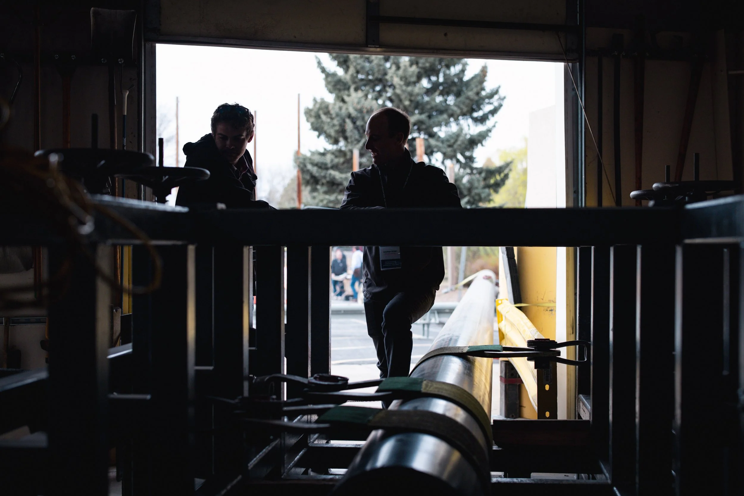 Silhouettes of two people standing in front of a large open garage door with outdoor trees and power lines visible in the background.