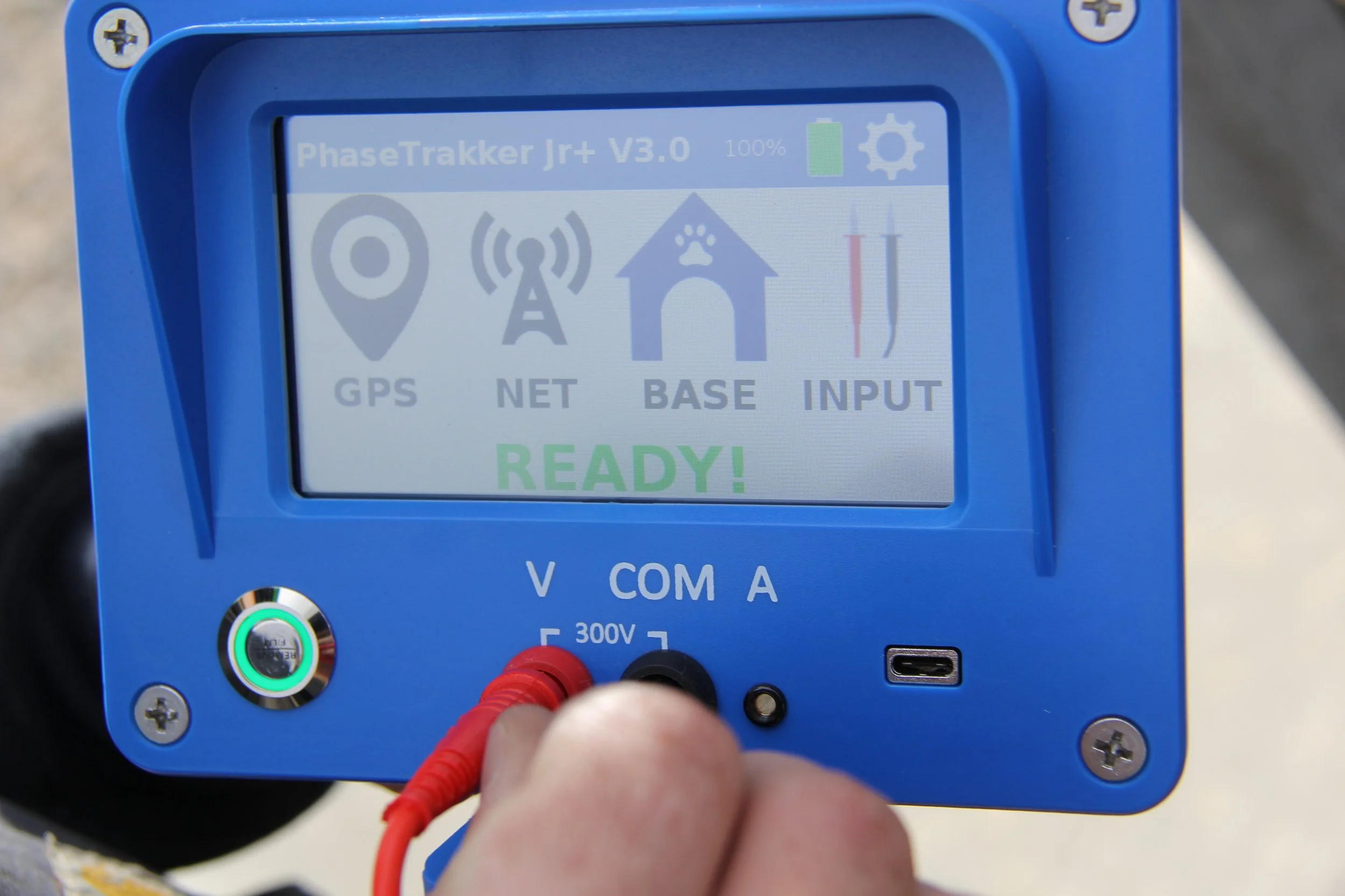 A blue electronic device with a display screen showing status icons and the word 'READY!' in green. The device has red and black cables connected to it and a USB port on the right side.
