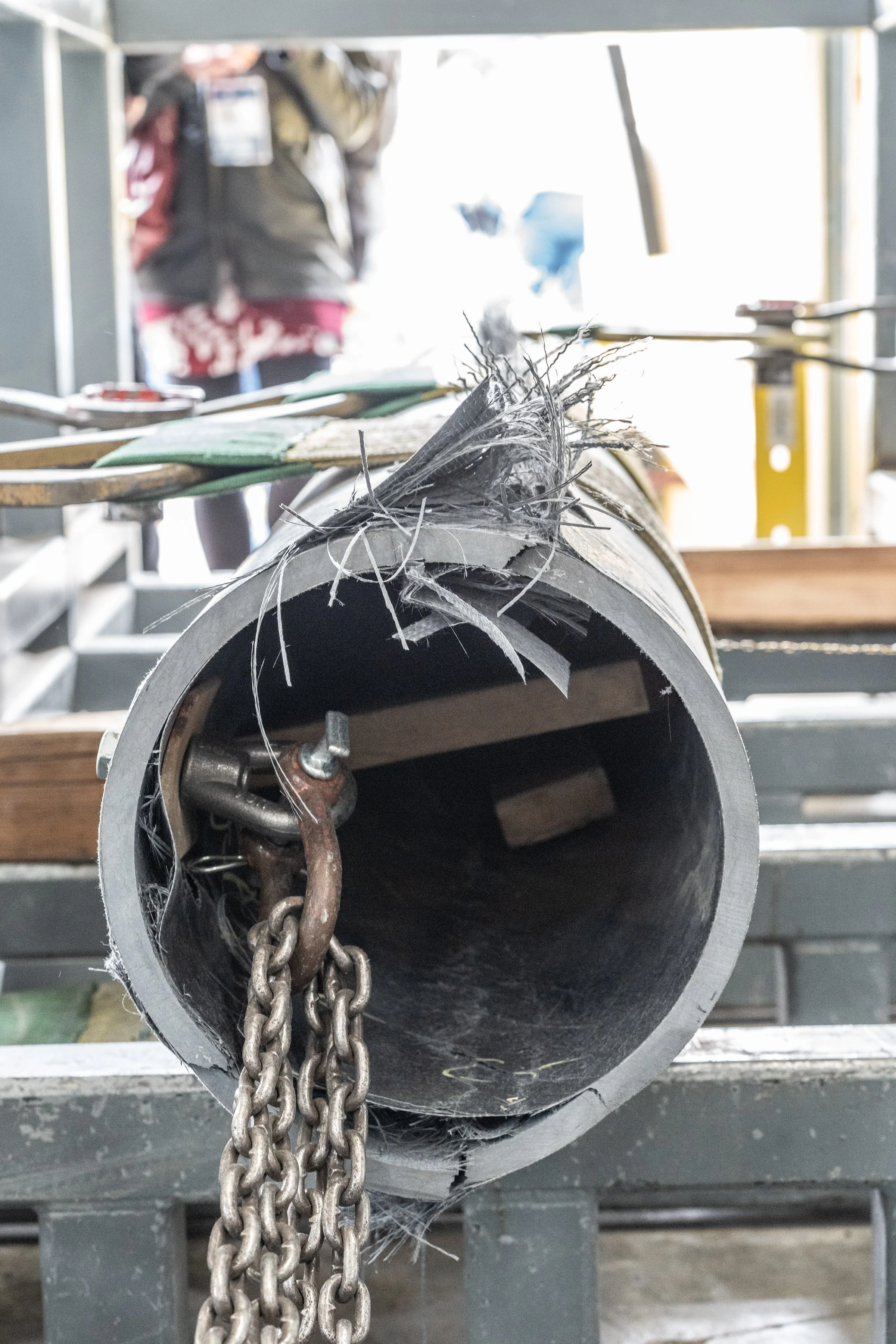 A large metal pipe with frayed wires and chains hanging out of it, on a metal table in a workshop.