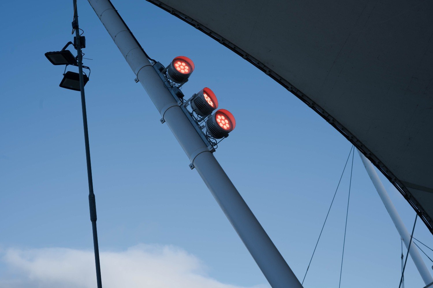 Minimalist shot of industrial red lights and white support beams against a clear blue sky at Dynamic Earth, Edinburgh.