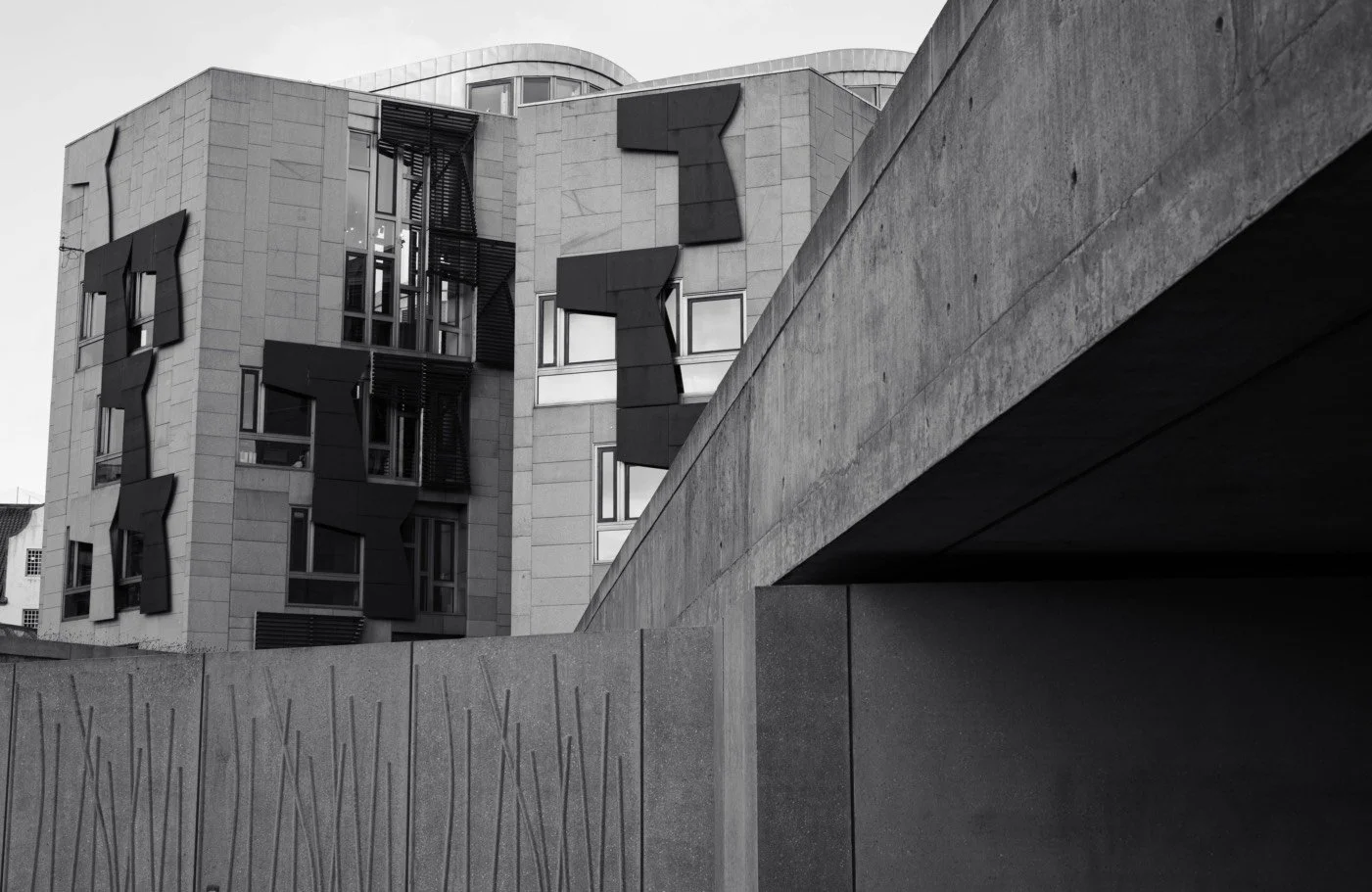 Black and white architectural photograph of the Scottish Parliament building, emphasizing geometric shapes and sharp shadows.