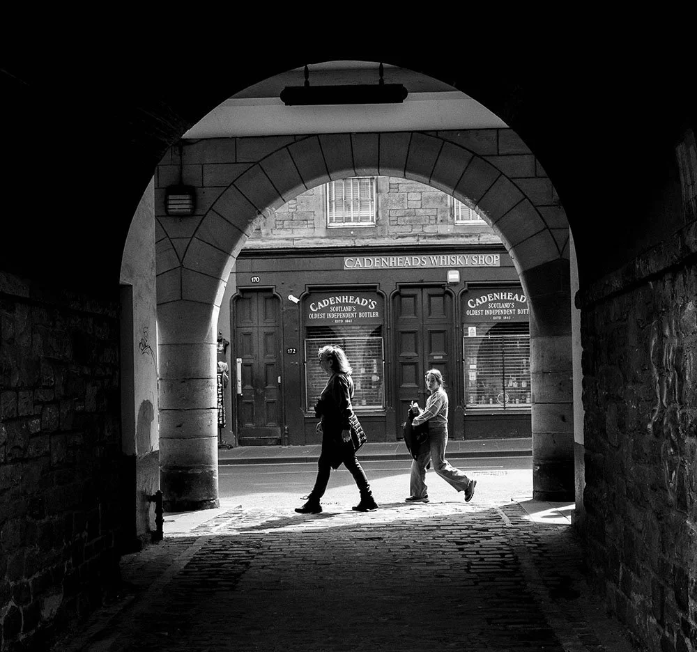 Image of people walking through a shard of light as walking past a close on Edinburgh's Royal Mile. Viewable on the Shutter Scotland 'Edinburgh Old Town Icons' photo walk.