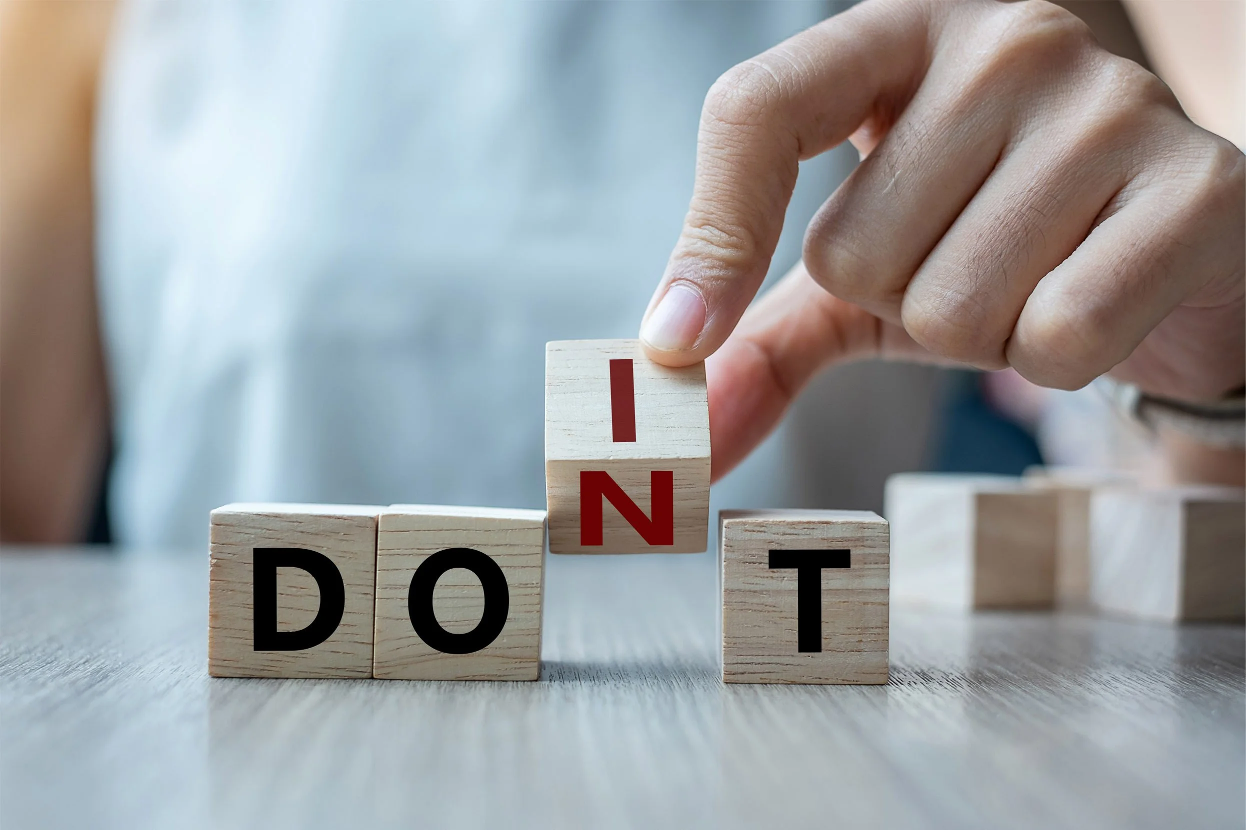 A person's hand arranging wooden blocks to spell the word "DON'T" on a table.