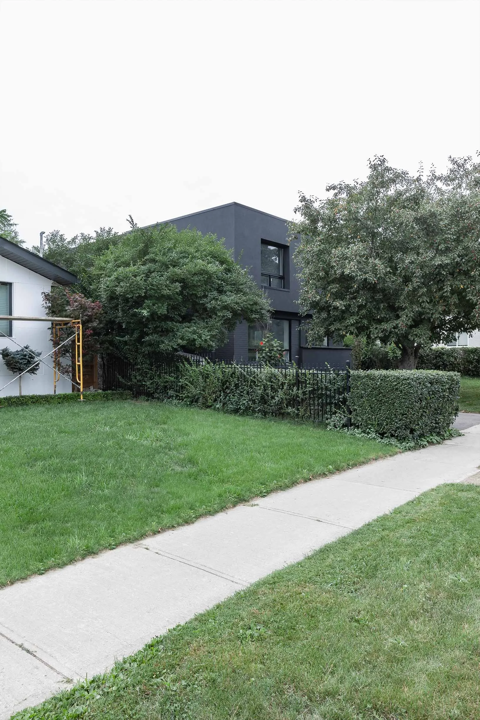 Ebenos House, exterior view in North York, Toronto, showing a modern black home with green lawn, trees, and sidewalk built by Maxamin Homes.