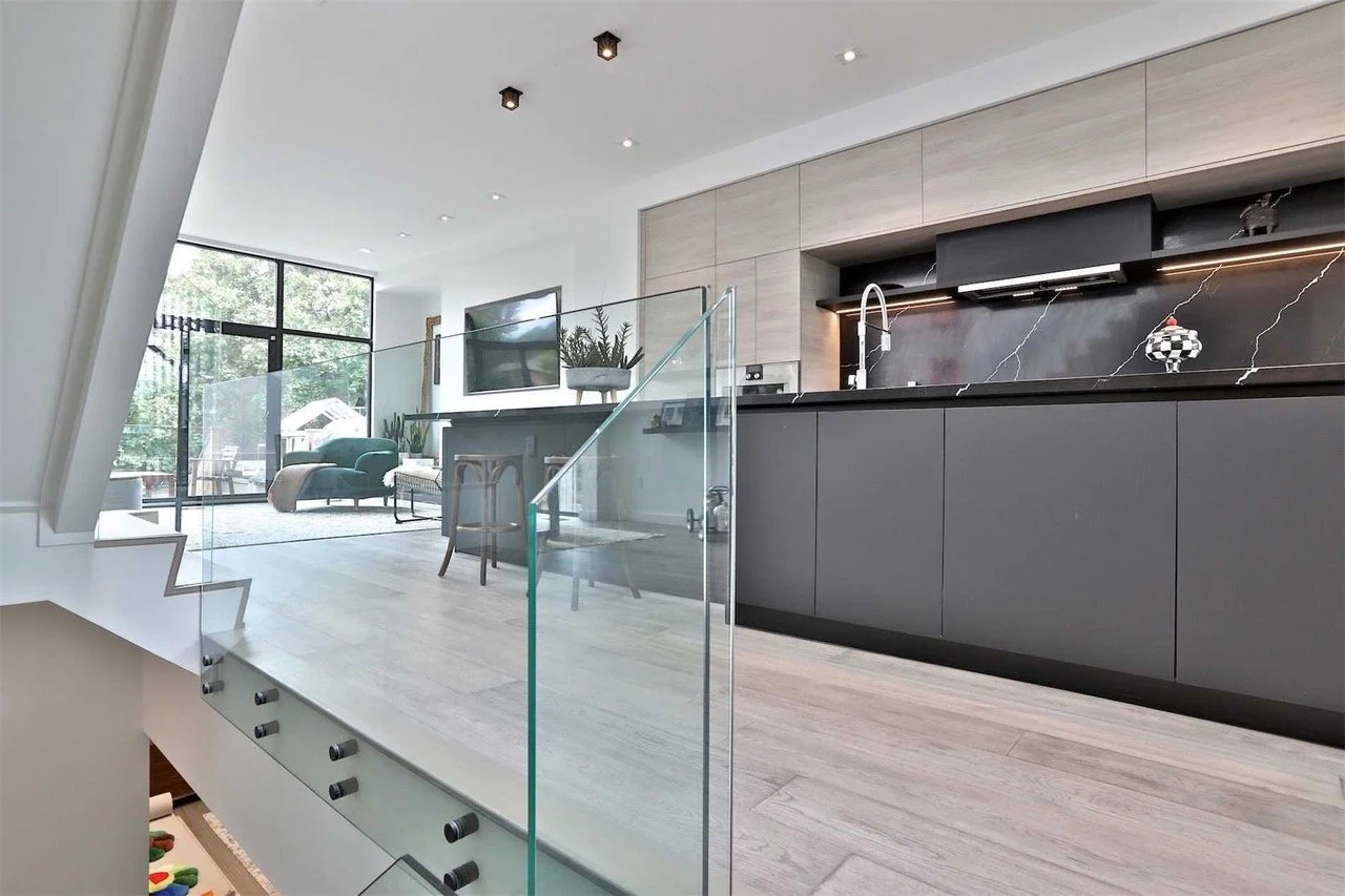 Modern open-concept living space with kitchen, sitting area, and large windows showing outdoor greenery.