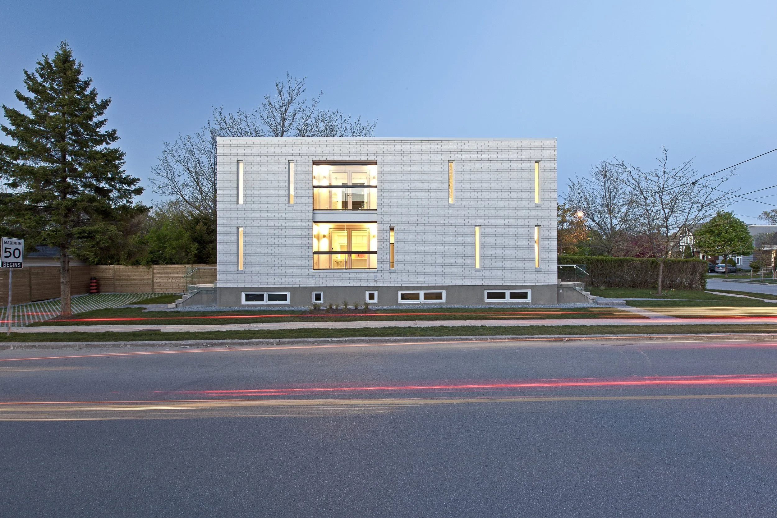 Patio House exterior in North York, Toronto, built by Maxamin Homes, white brick home with glowing windows and light trails from cars at night.