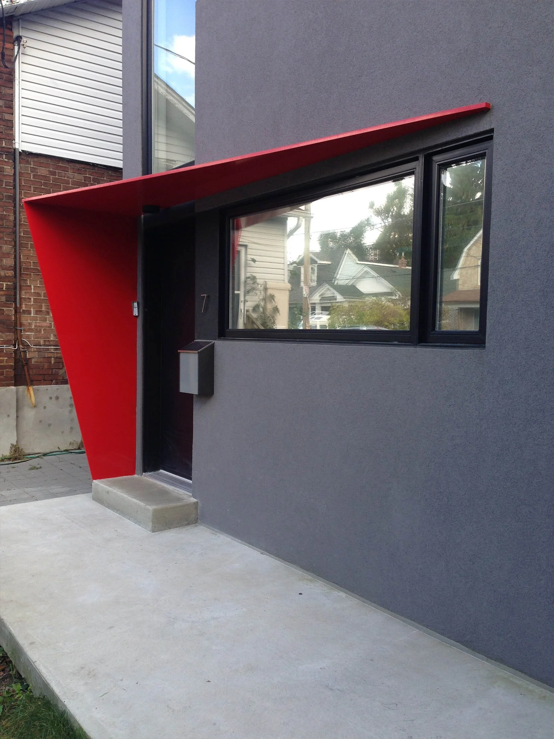 Whale House exterior in East York, Toronto, built by Maxamin Homes, with gray wall, black-framed window, black door, and red angular awning.