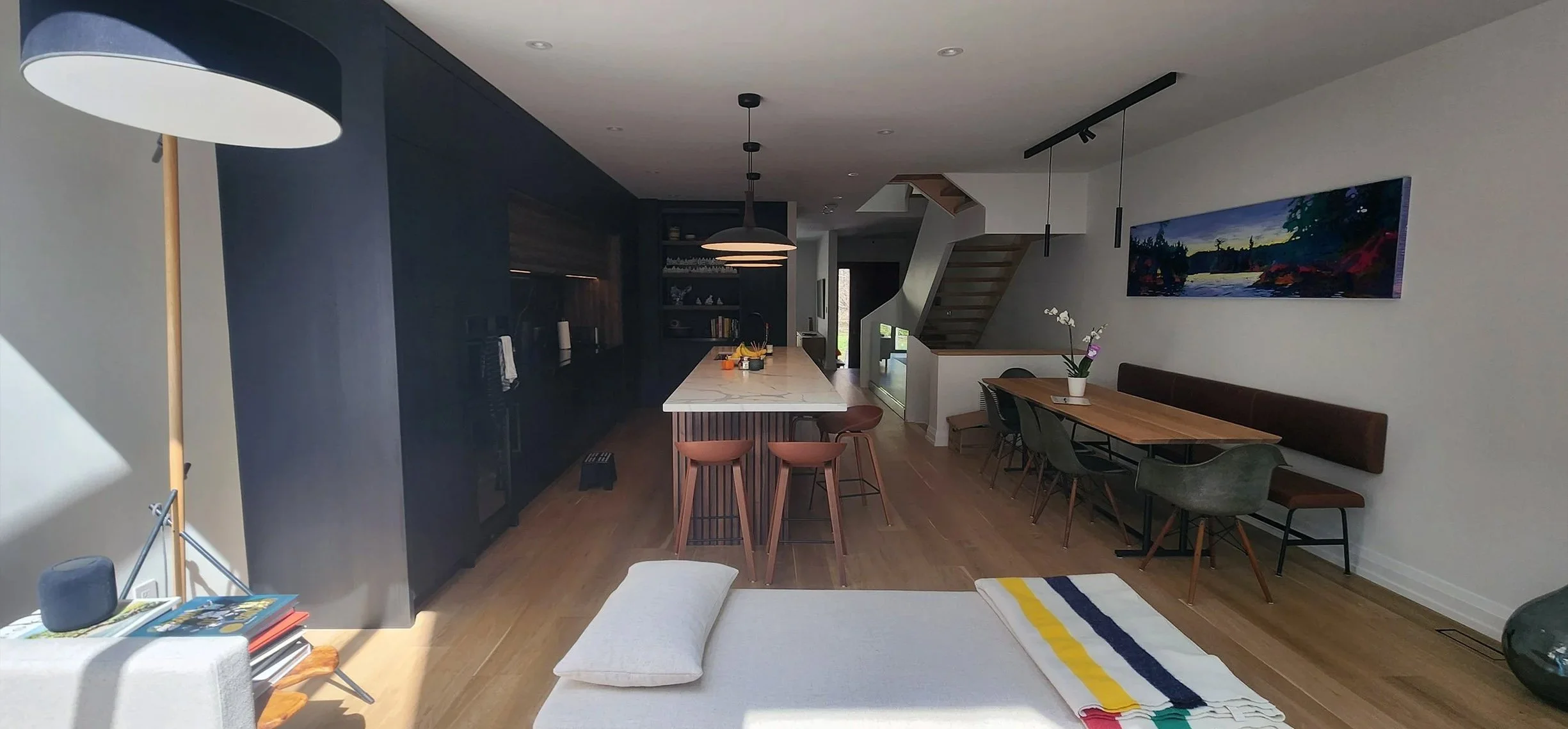 Lantern House dining area in The Beaches, Toronto, built by Maxamin Homes, with wooden table, bench seating, potted plant, and colorful artwork.
