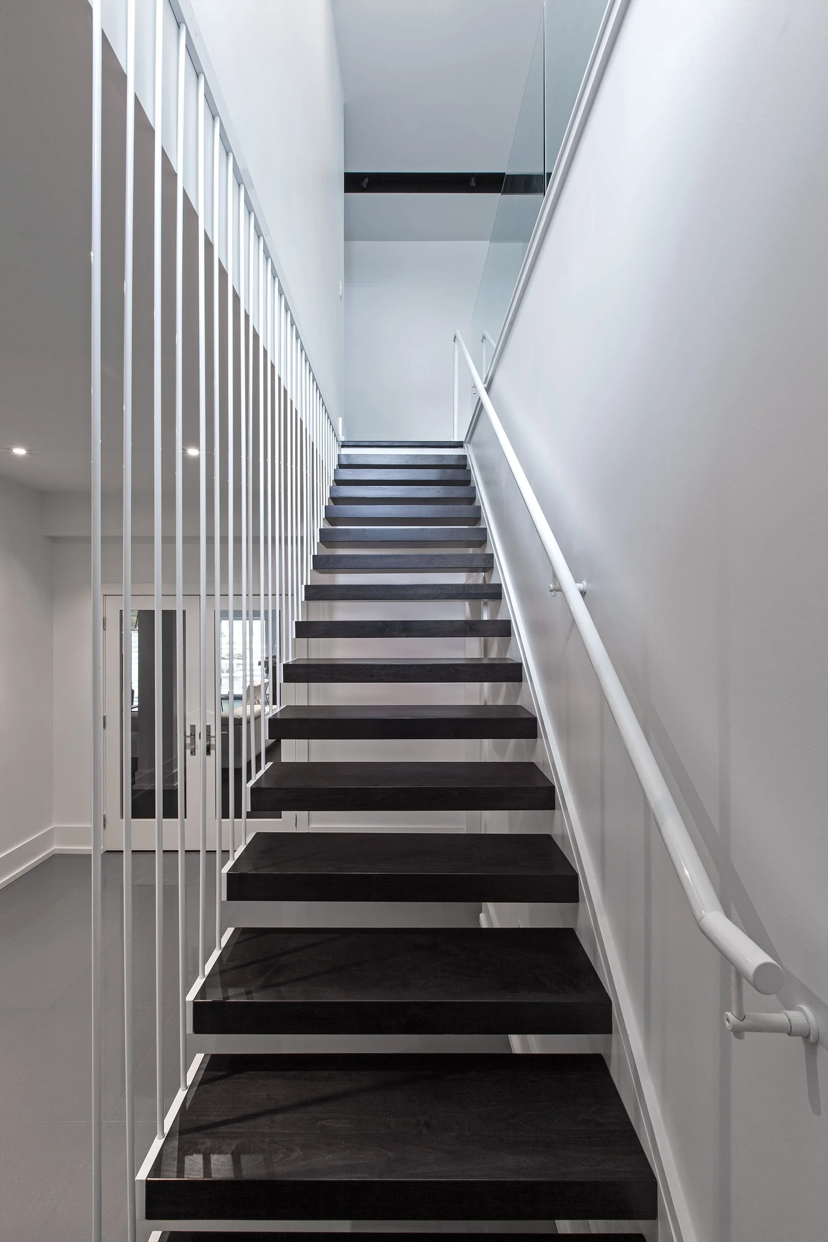 Gallery House staircase in East York, Toronto, built by Maxamin Homes, with dark wood steps, glass panels, and modern white minimalist interior.
