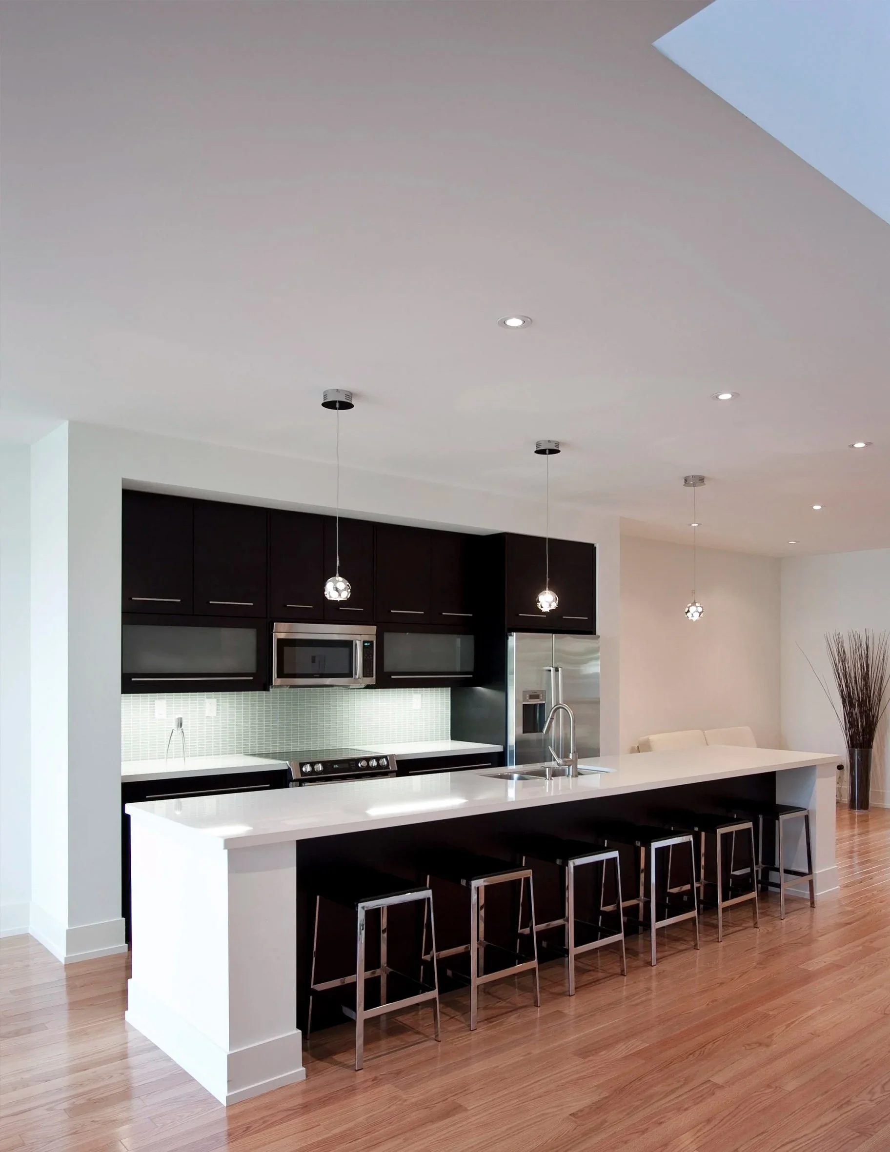 63˚ House kitchen in East York, Toronto, built by Maxamin Homes, with black cabinets, white island countertop, pendant lights, and wooden flooring.