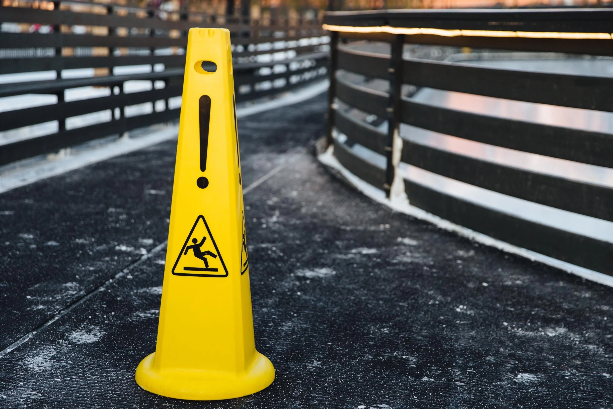 Yellow caution cone with a wet surface and a black barricade on a footbridge or pathway, indicating a slippery or hazardous area.