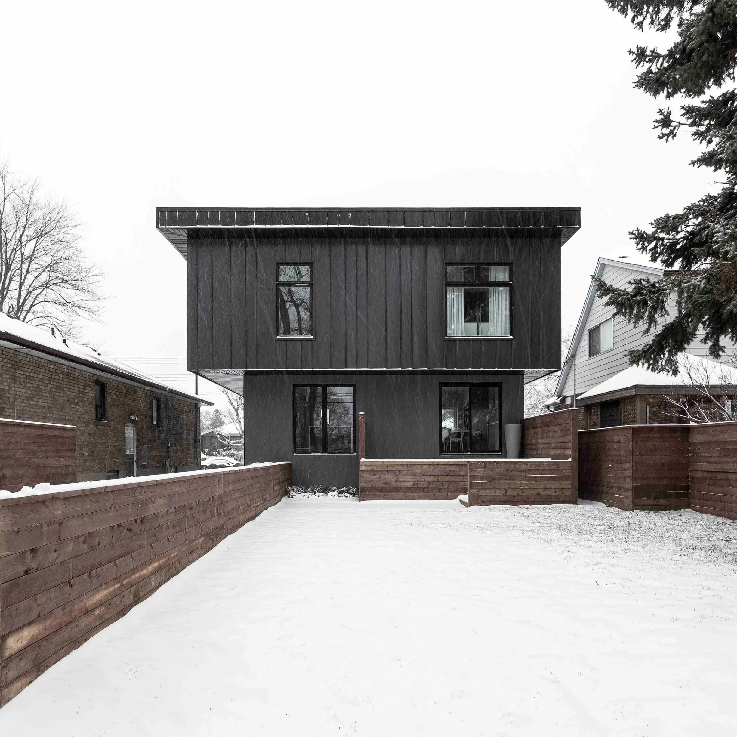 Albers House exterior in Scarborough, Toronto, built by Maxamin Homes, dark two-story design with large windows, wooden fence, and snow.
