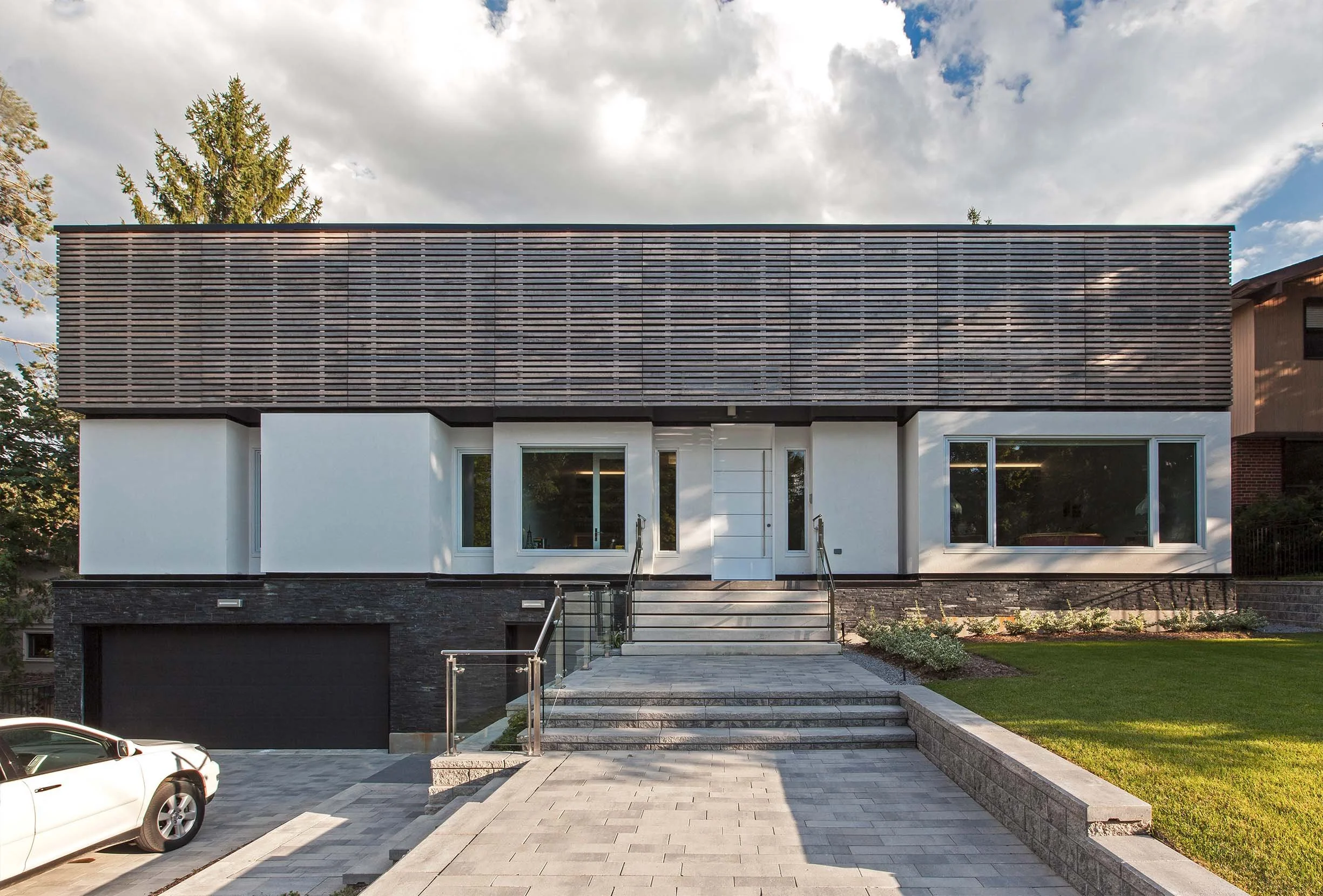 Gallery House exterior in East York, Toronto, built by Maxamin Homes, two-story home with white walls, black garage, wood facade, and landscaped yard.