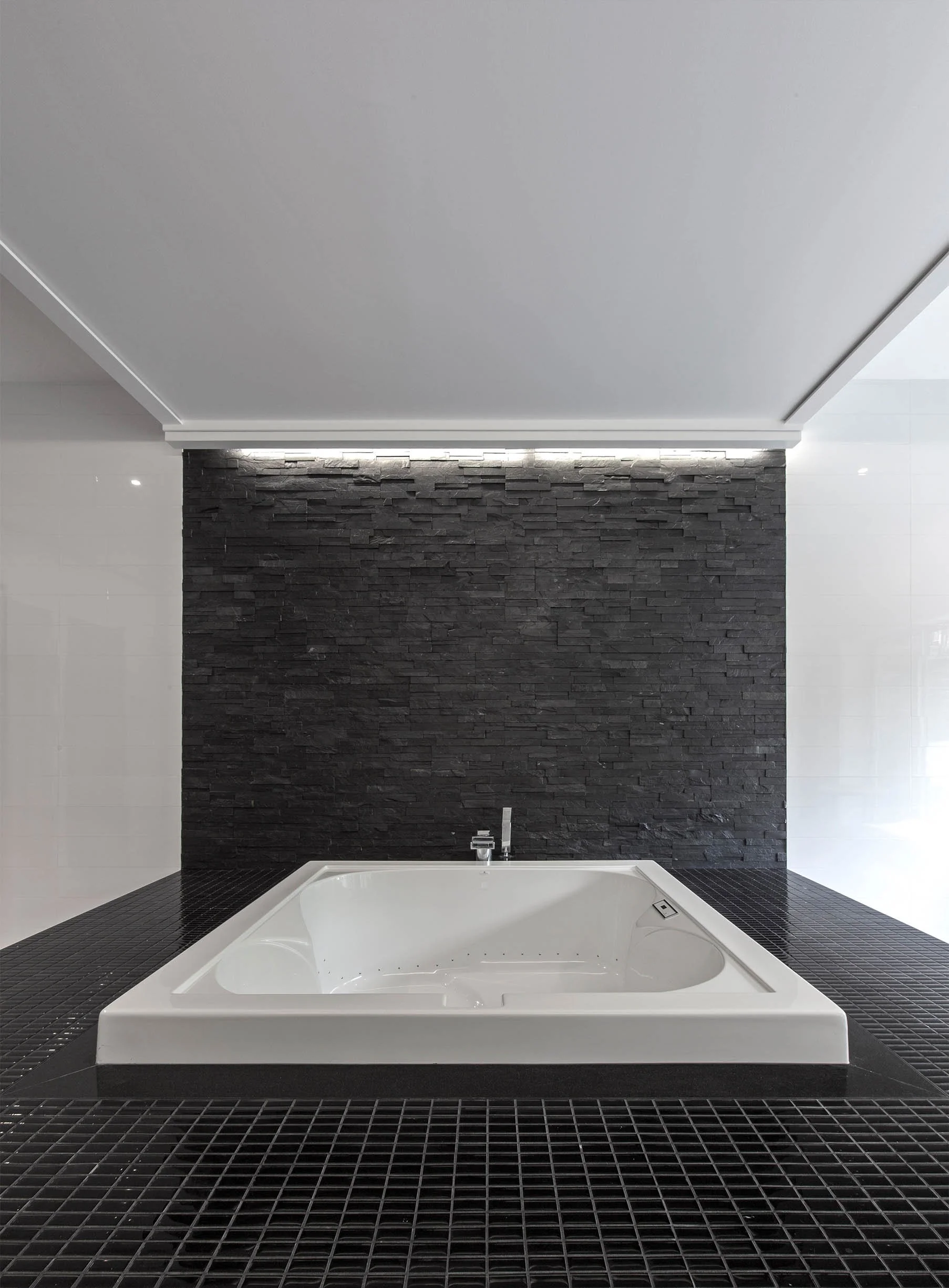 Gallery House bathroom in East York, Toronto, built by Maxamin Homes, with white bathtub, black stone wall, dark floor tiles, and soft ceiling lighting.
