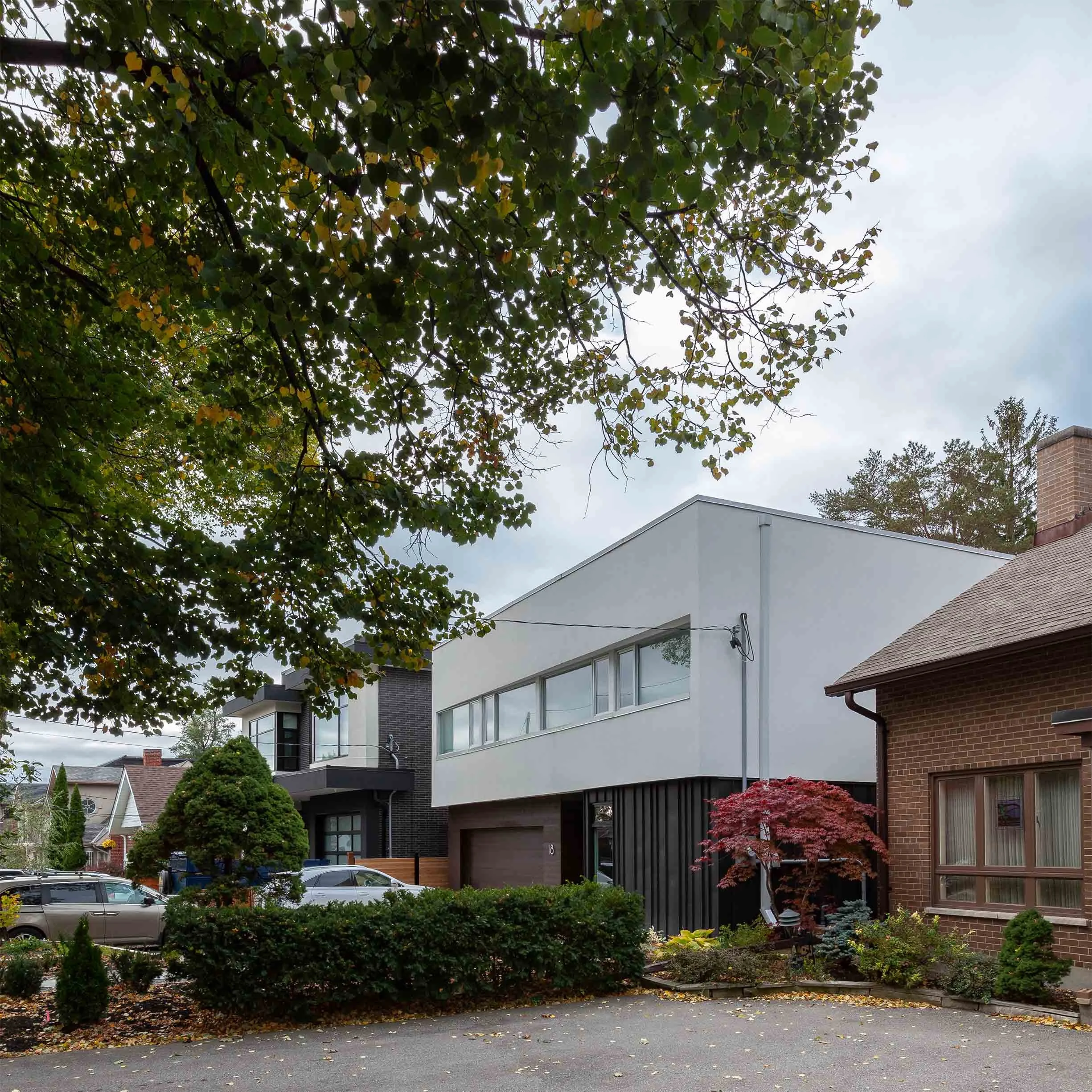 Fun House, a modern white custom home in East York, Toronto, built by Maxamin Homes, surrounded by trees and plants in a suburban neighborhood.