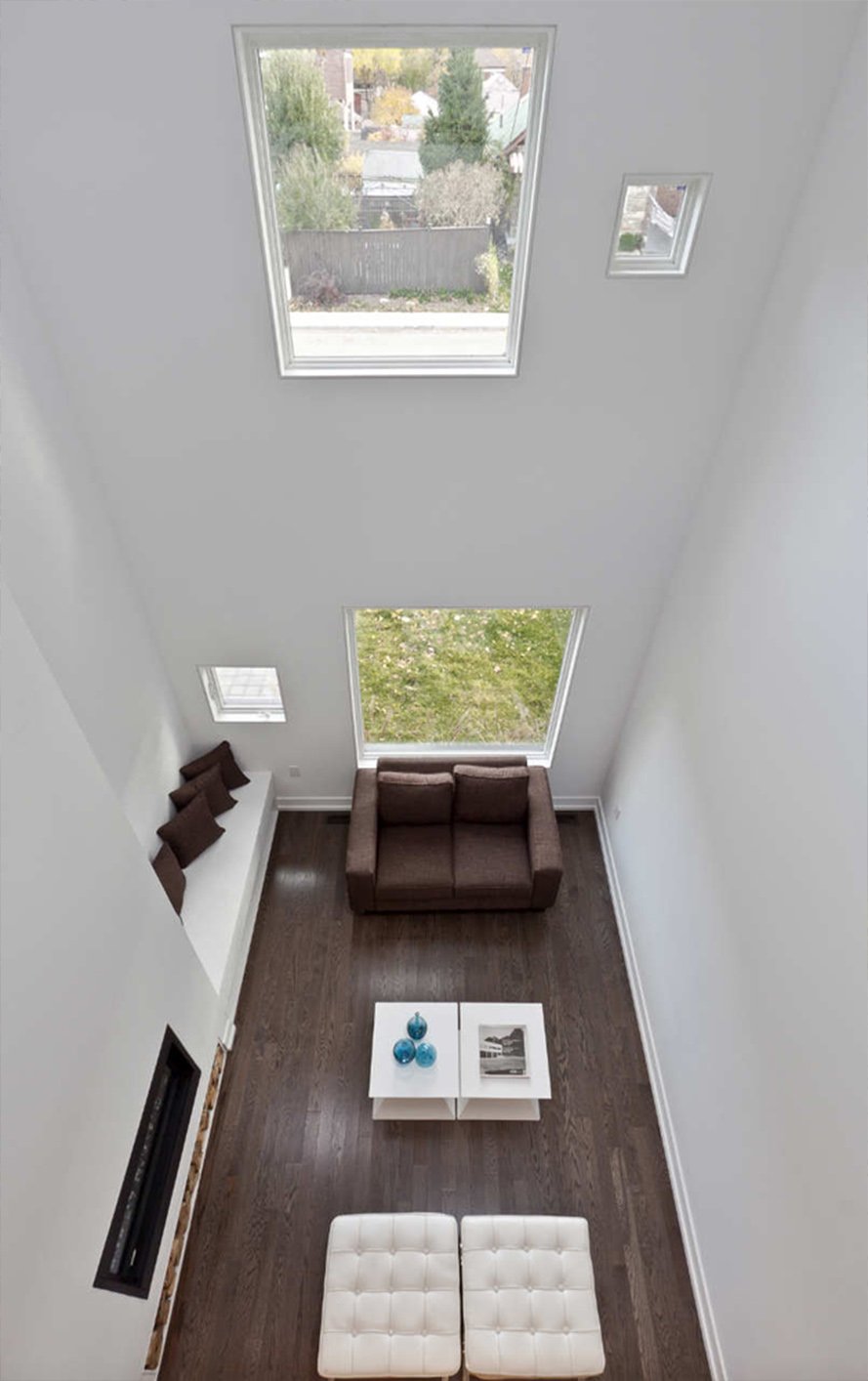 Charcoal House living room in East York, Toronto, built by Maxamin Homes, featuring vaulted ceiling, skylights, fireplace, and brown sofa.