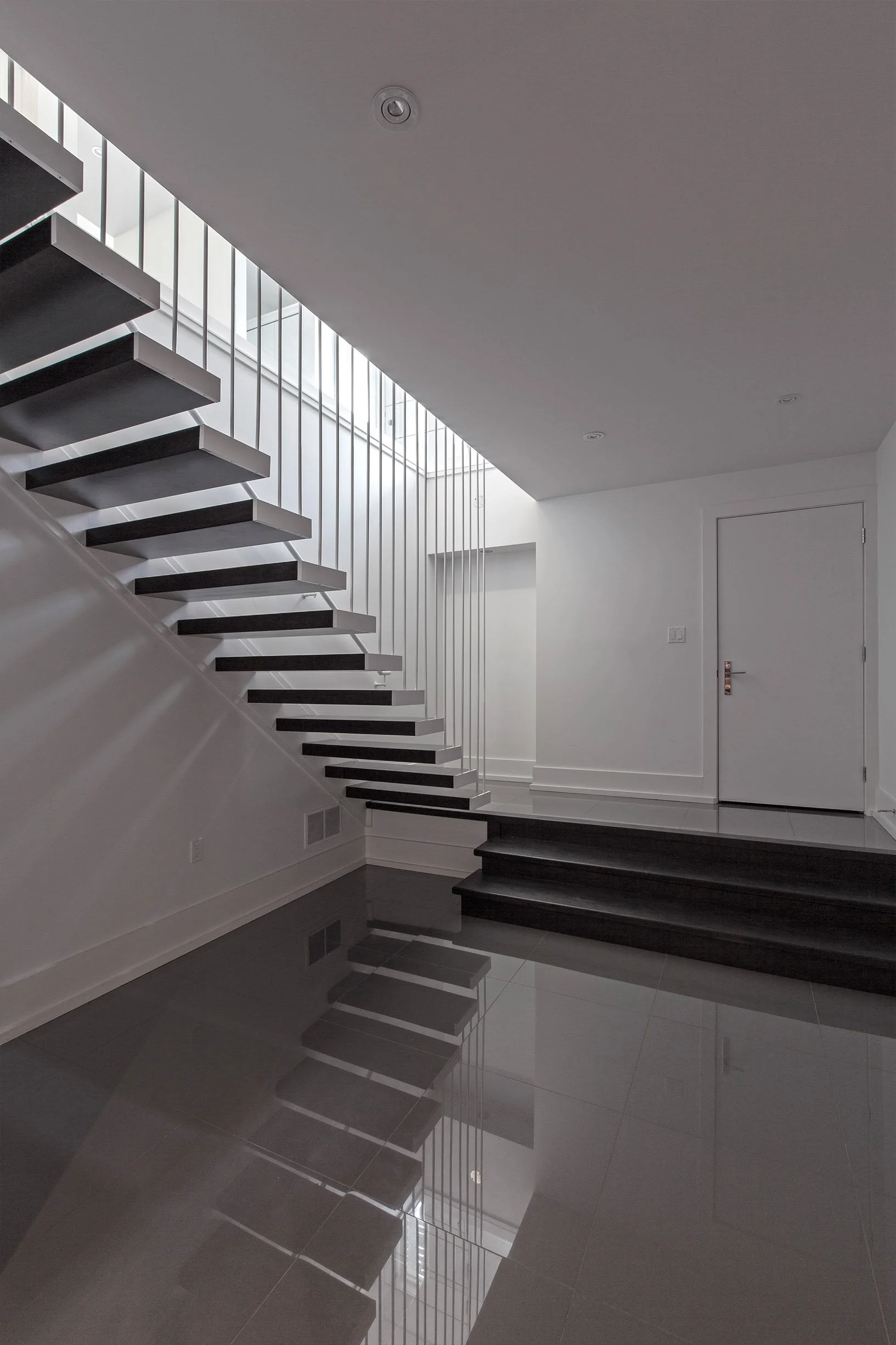 Gallery House staircase in East York, Toronto, built by Maxamin Homes, with dark treads, metal railing, and minimalist white interior.
