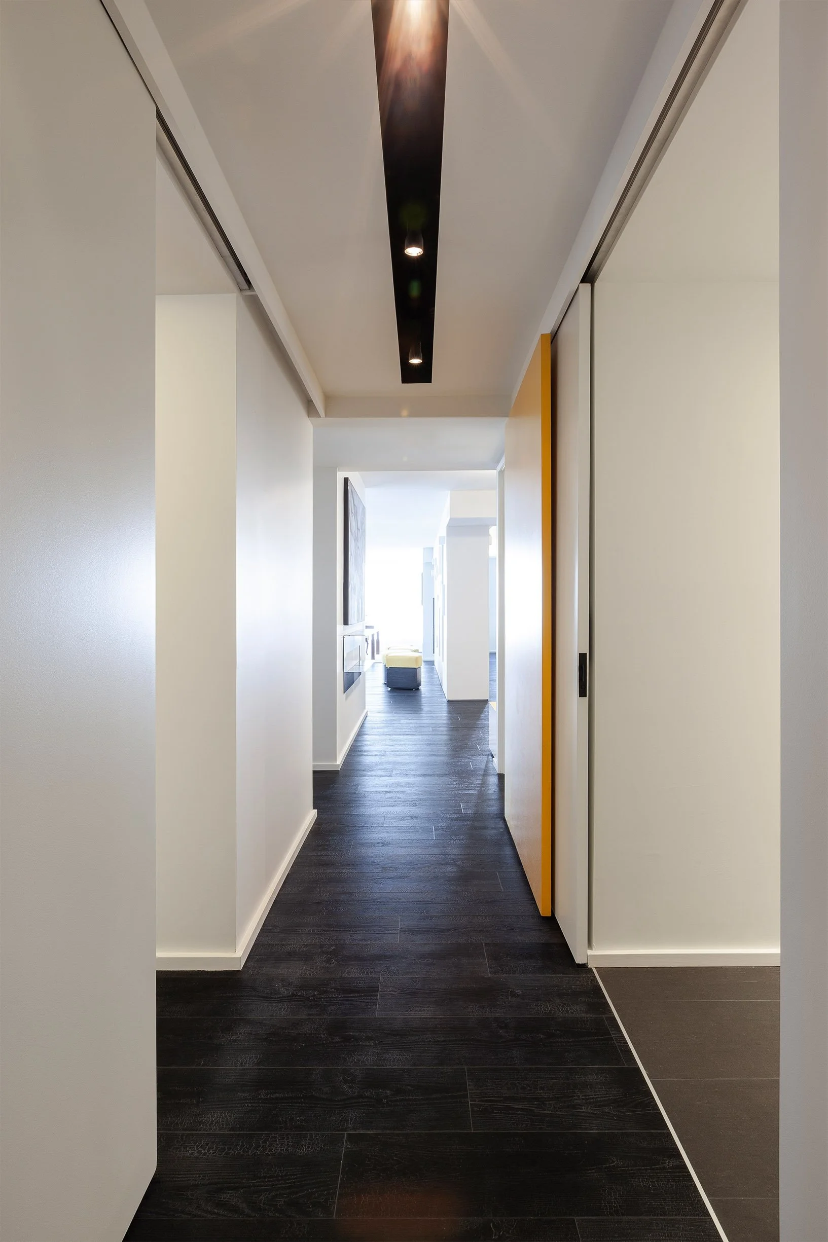 DOHA Nest hallway in North York, Toronto, built by Maxamin Homes, featuring dark wood floors, black ceiling panel with lights, and yellow sliding door.