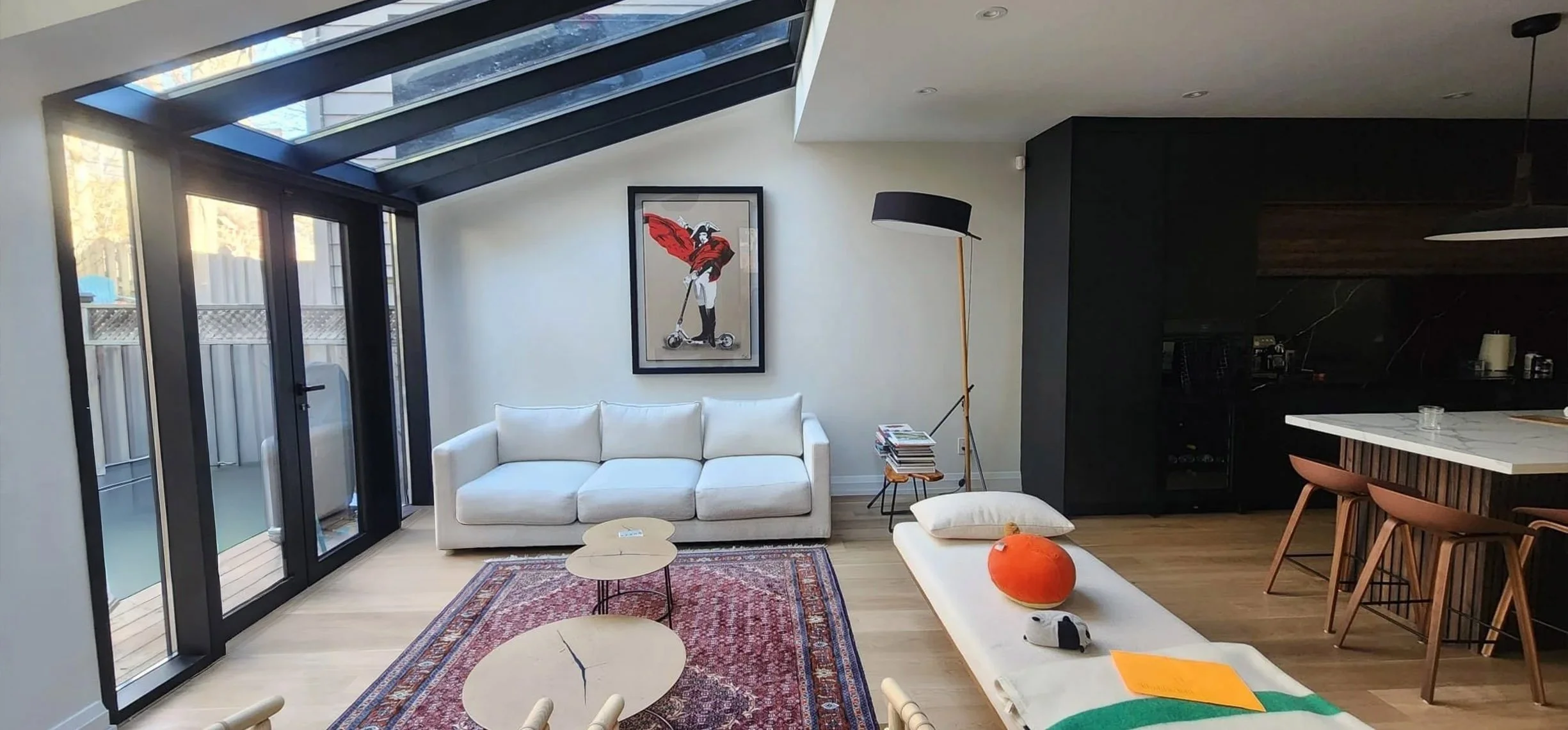 Lantern House living room in The Beaches, Toronto, built by Maxamin Homes, with white sofa, artwork of woman on scooter, and glass doors to patio.