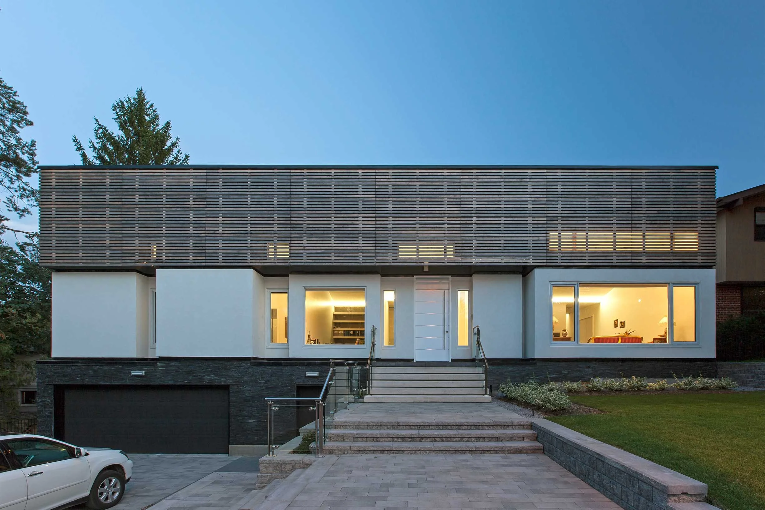 Gallery House exterior in East York, Toronto, built by Maxamin Homes, with white walls, wood siding, and illuminated front entrance at dusk.