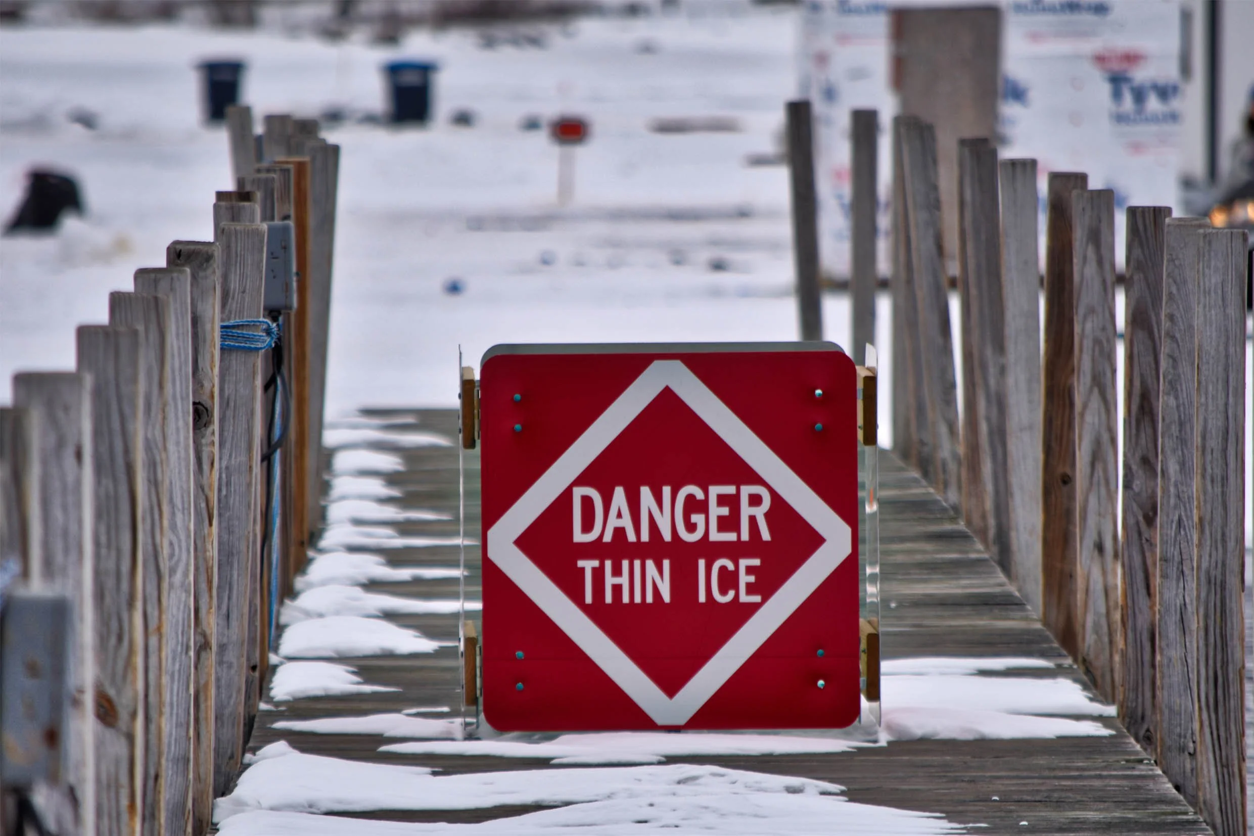 Warning sign on a snowy dock walkway stating 'Danger Thin Ice'