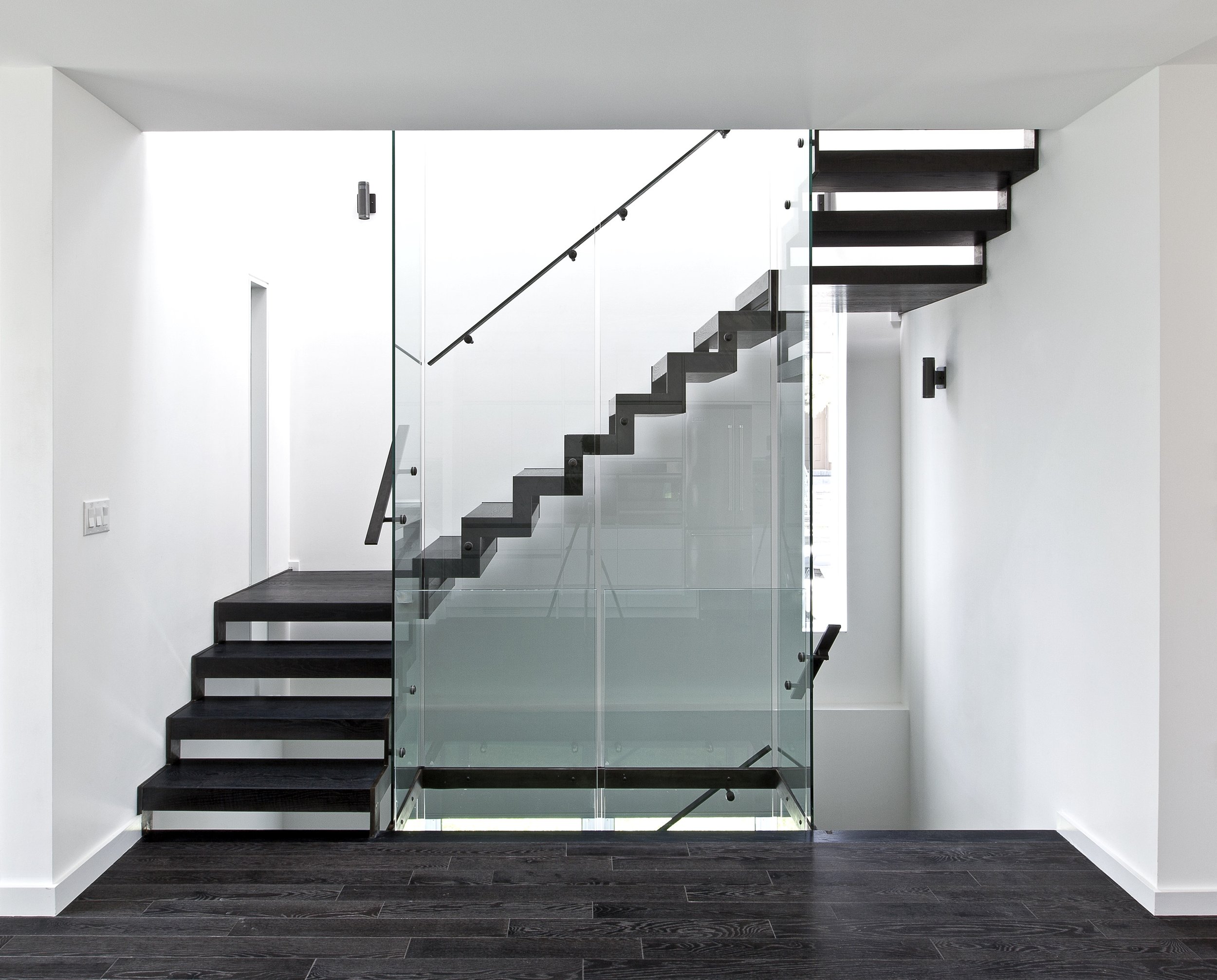 Patio House staircase in North York, Toronto, built by Maxamin Homes, featuring black steps, glass railing, and white minimalist walls.