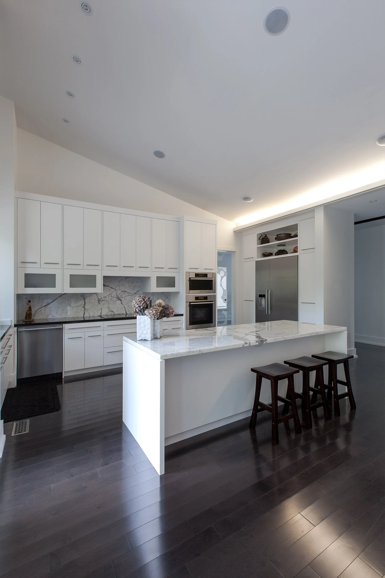 Gallery House kitchen in East York, Toronto, built by Maxamin Homes, featuring marble island, black stools, white cabinets, and stainless appliances.