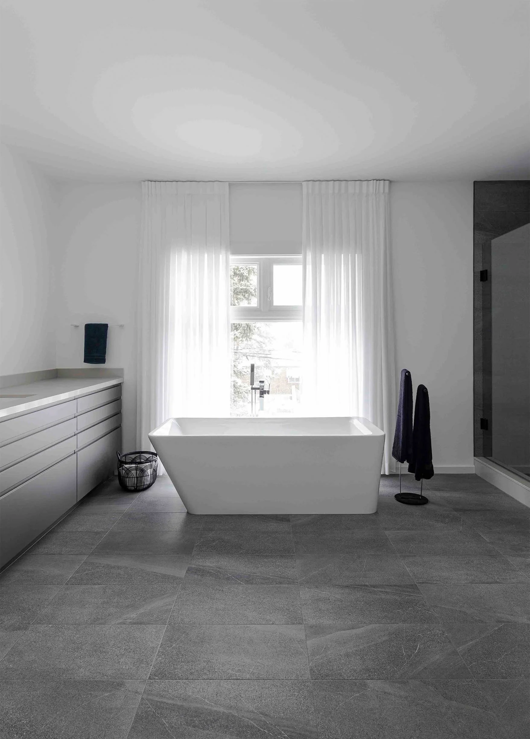 Albers House bathroom in Scarborough, Toronto, built by Maxamin Homes, with white bathtub, gray tile floor, and minimalist white walls.