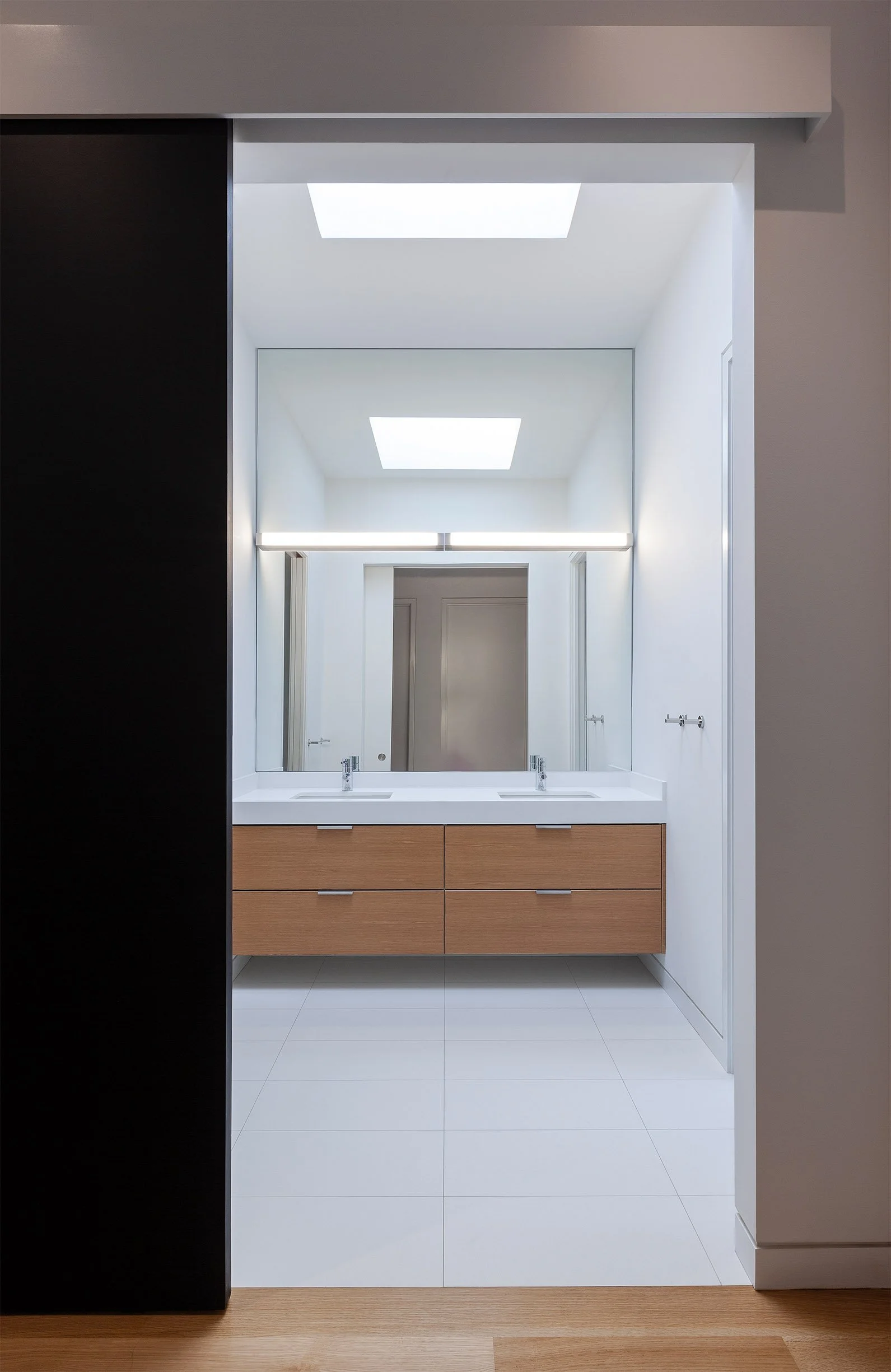 Fun House bathroom in East York, Toronto, built by Maxamin Homes, featuring double sinks, wooden vanity, skylights, and minimalist white walls.