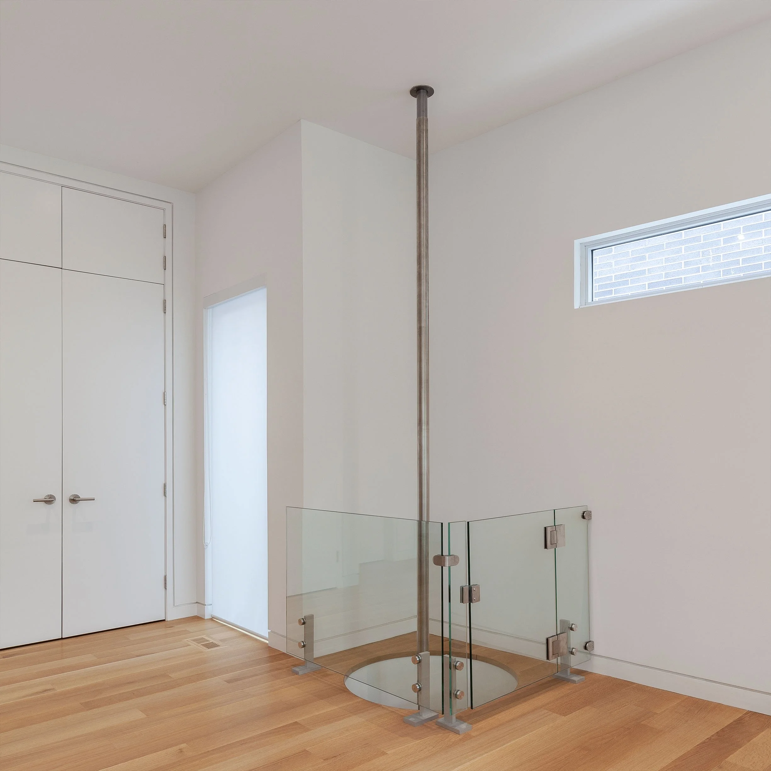 Fun House upper floor interior in East York, Toronto, built by Maxamin Homes, with glass railing, spiral staircase opening, and white minimalist design.