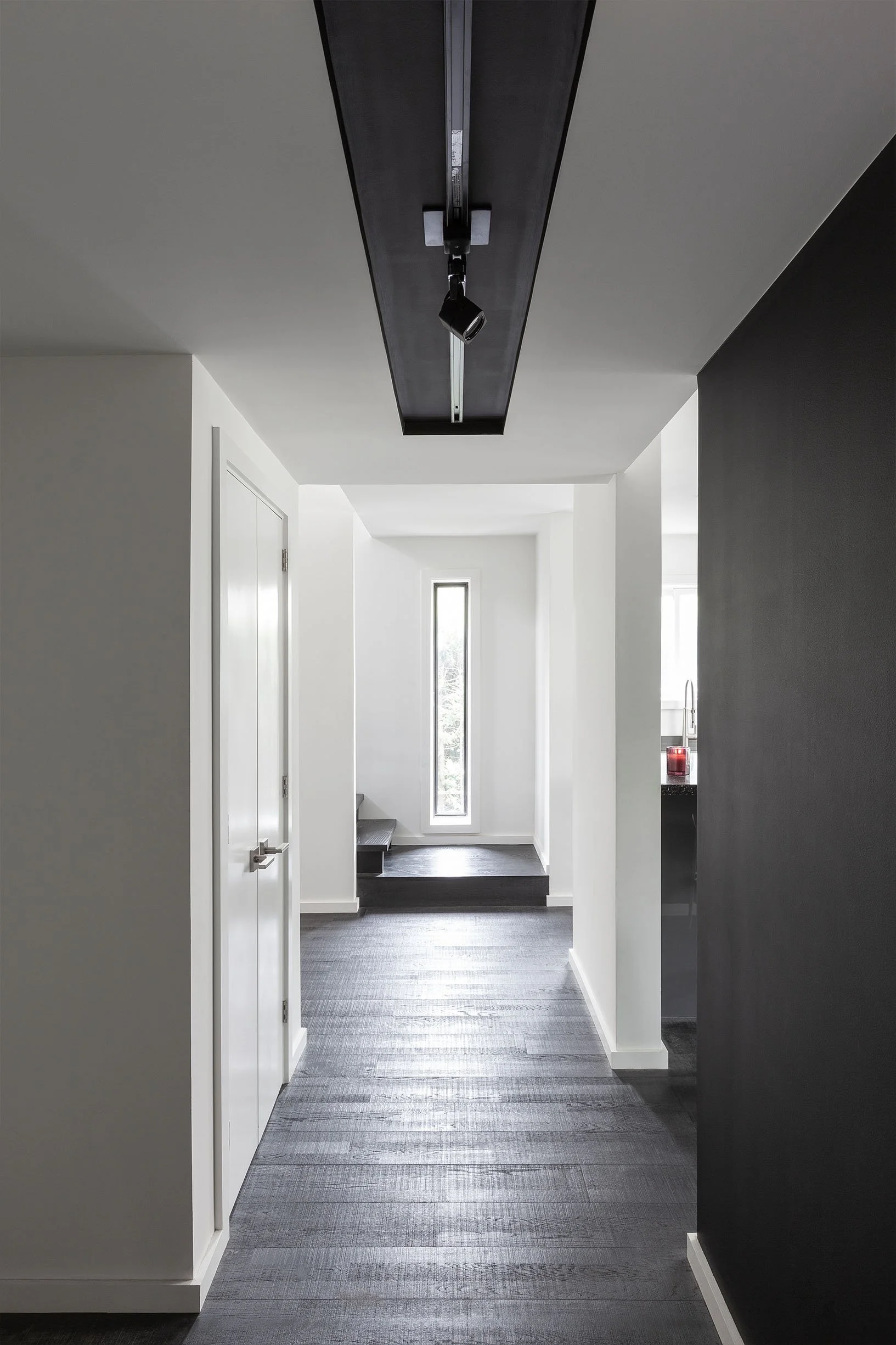 Ebenos House, a minimalist hallway in North York, Toronto, with white walls, dark flooring, and a black ceiling detail with a light fixture built by Maxamin Homes.
