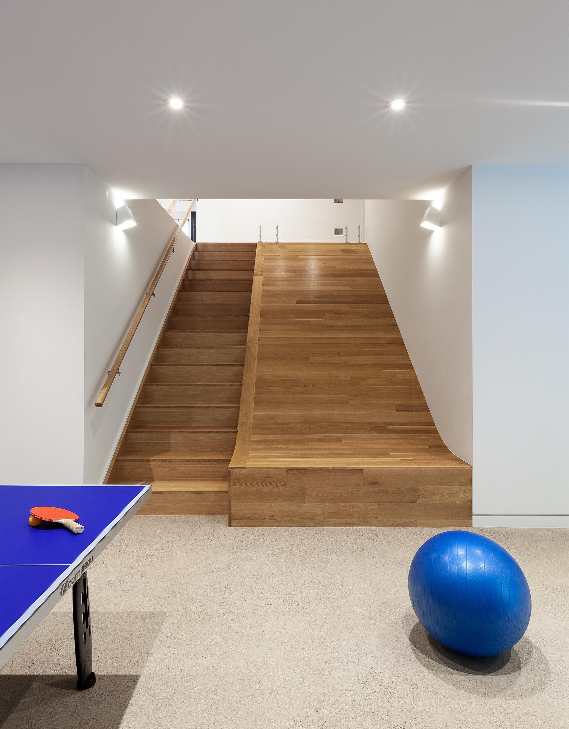 Fun House recreation area in East York, Toronto, built by Maxamin Homes, with wooden stairs, ping pong table, blue exercise ball, and white walls.