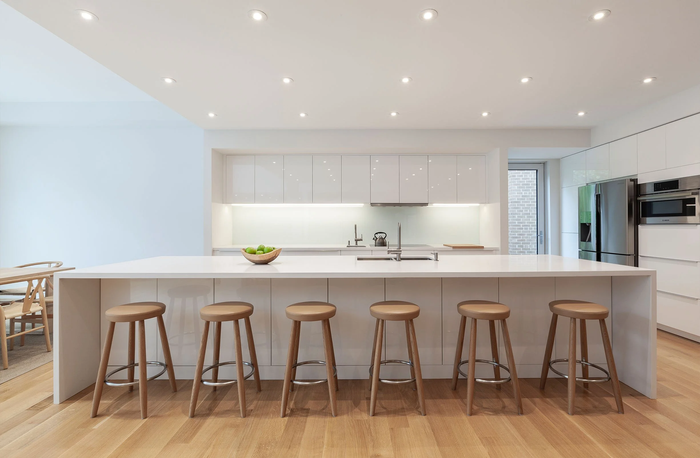 Fun House kitchen in East York, Toronto, built by Maxamin Homes, with white cabinets, large island, six wooden stools, and stainless steel appliances.