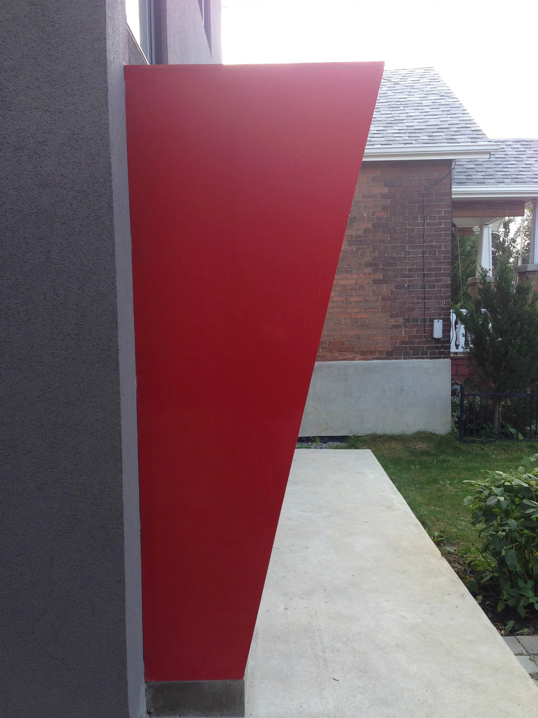 Whale House architectural detail in East York, Toronto, built by Maxamin Homes, showing red angular element on gray wall with grass and walkway.