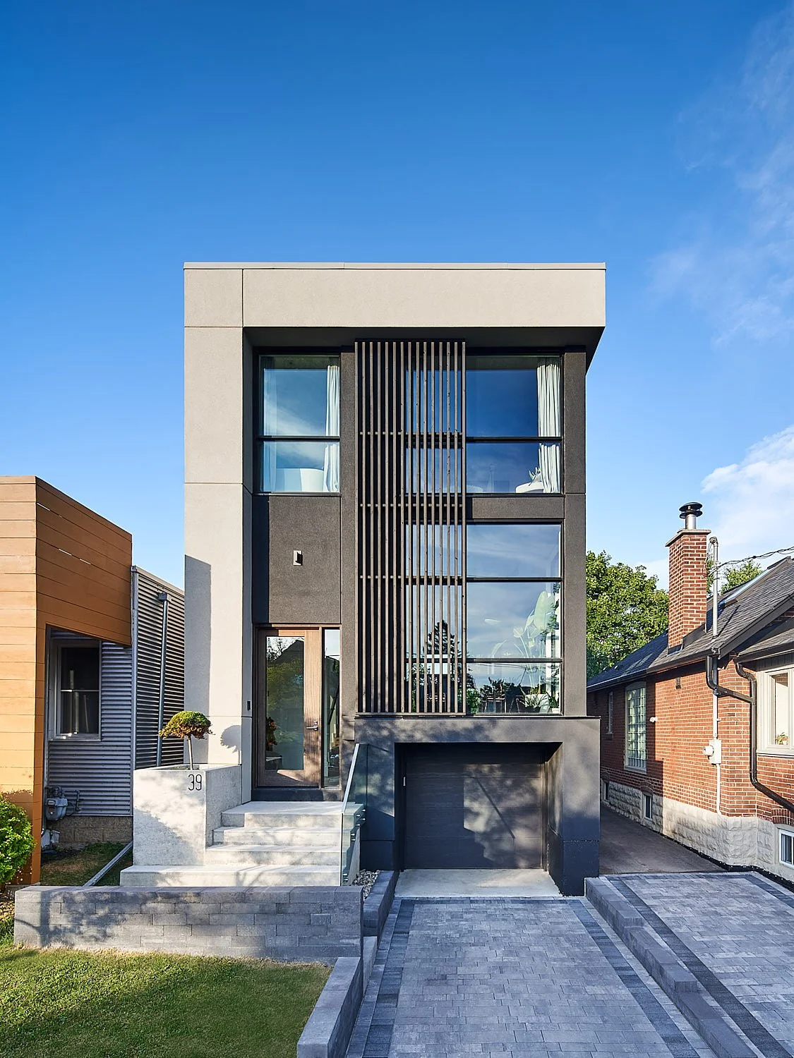 Romeo’s House, a modern luxury custom home in Etobicoke, Toronto, built by Maxamin Homes, featuring a three-story design with large glass windows, exterior lighting, and a concrete staircase at dusk.