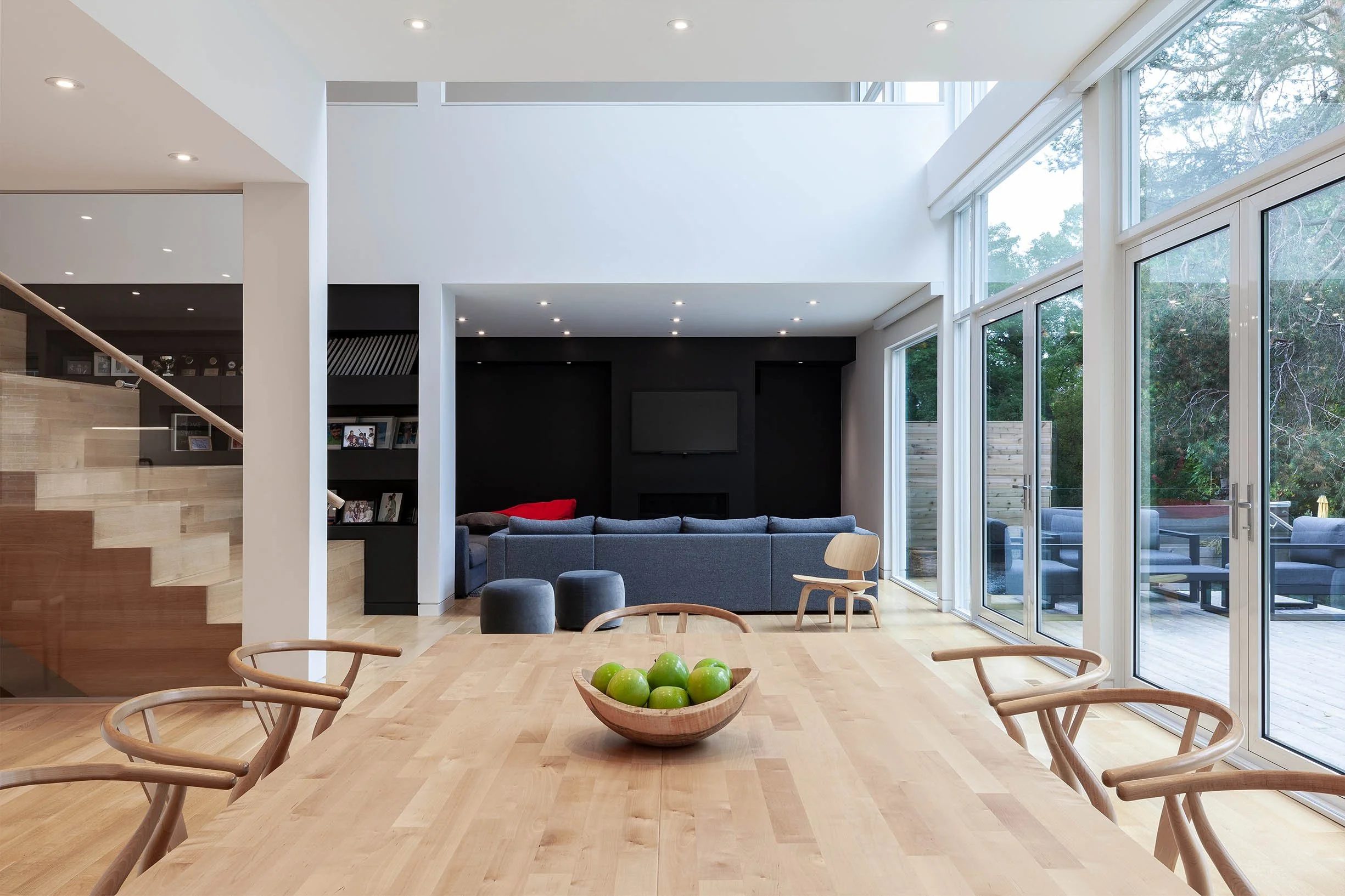 Fun House living room in East York, Toronto, built by Maxamin Homes, with dining table, gray sofa, black accent wall, and patio access with seating.