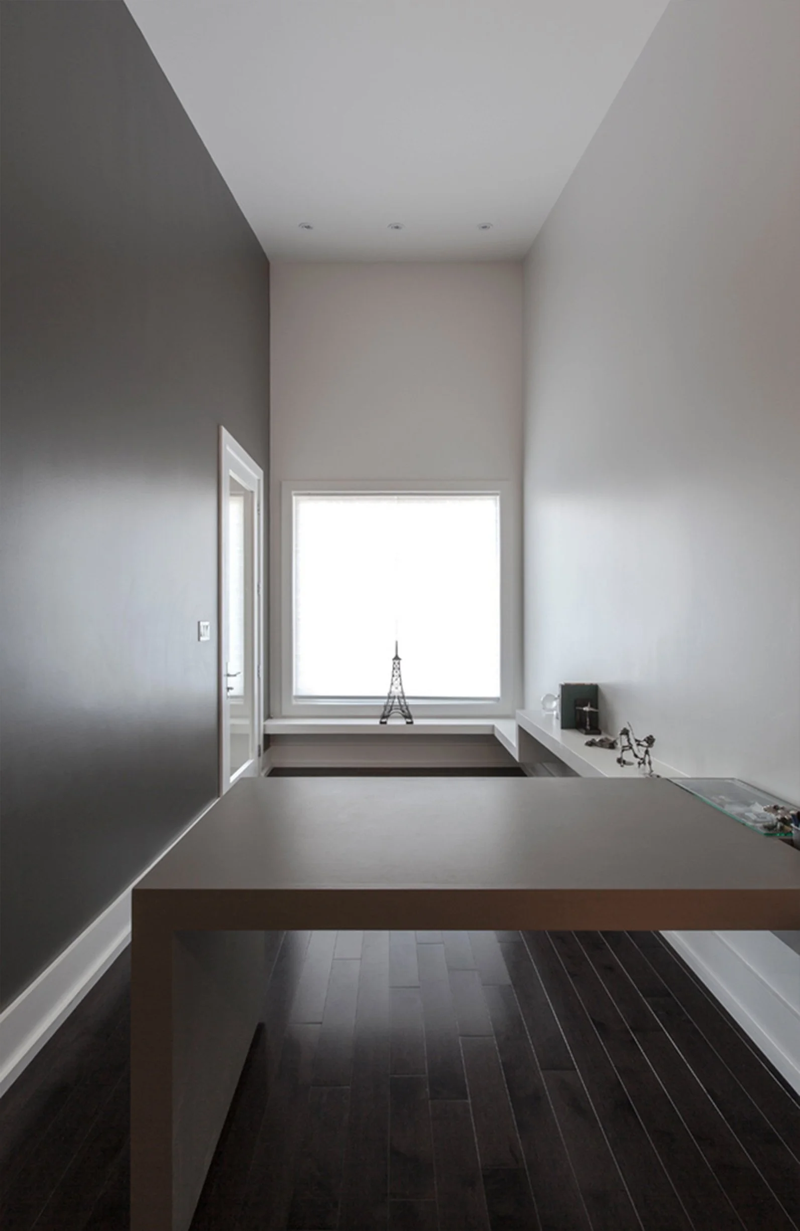 Minimalist modern workspace with a large window, white walls, dark wood flooring, and a white desk.