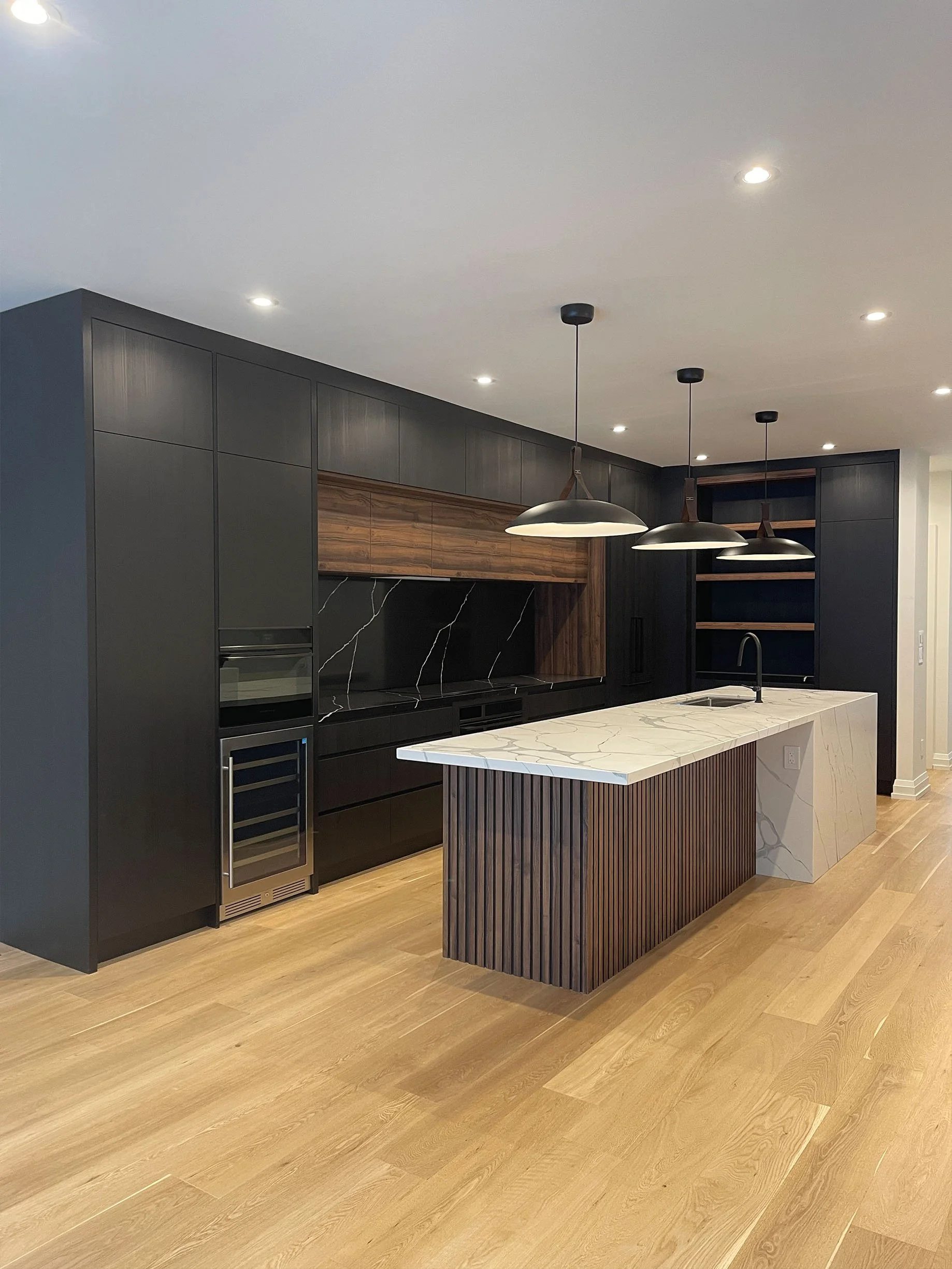 Modern kitchen with black cabinets, marble island, wooden accents, and pendant lighting.