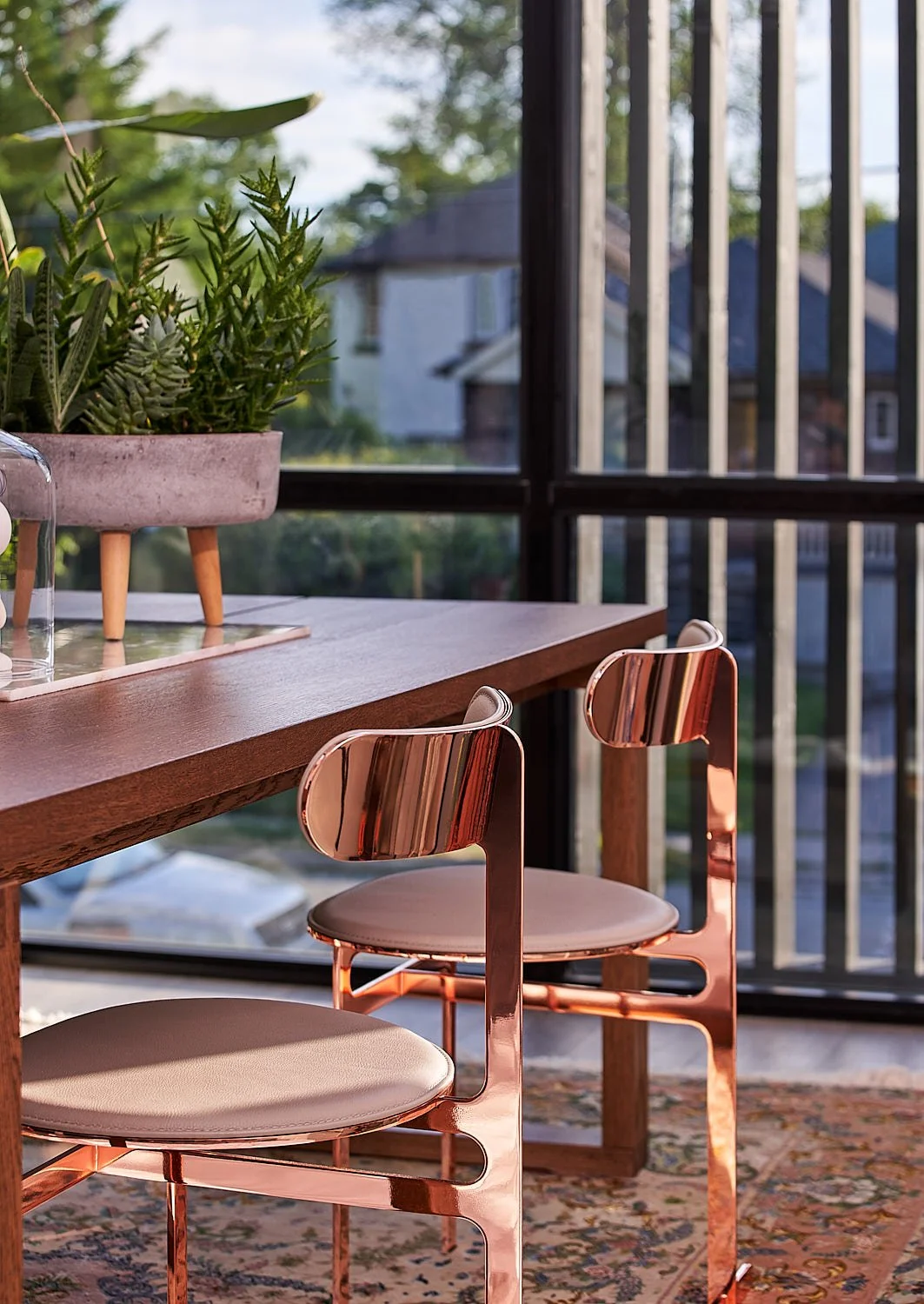 Romeo’s House dining area in Etobicoke, Toronto, built by Maxamin Homes, featuring wooden table, copper chairs, potted plant, and large black-framed windows.