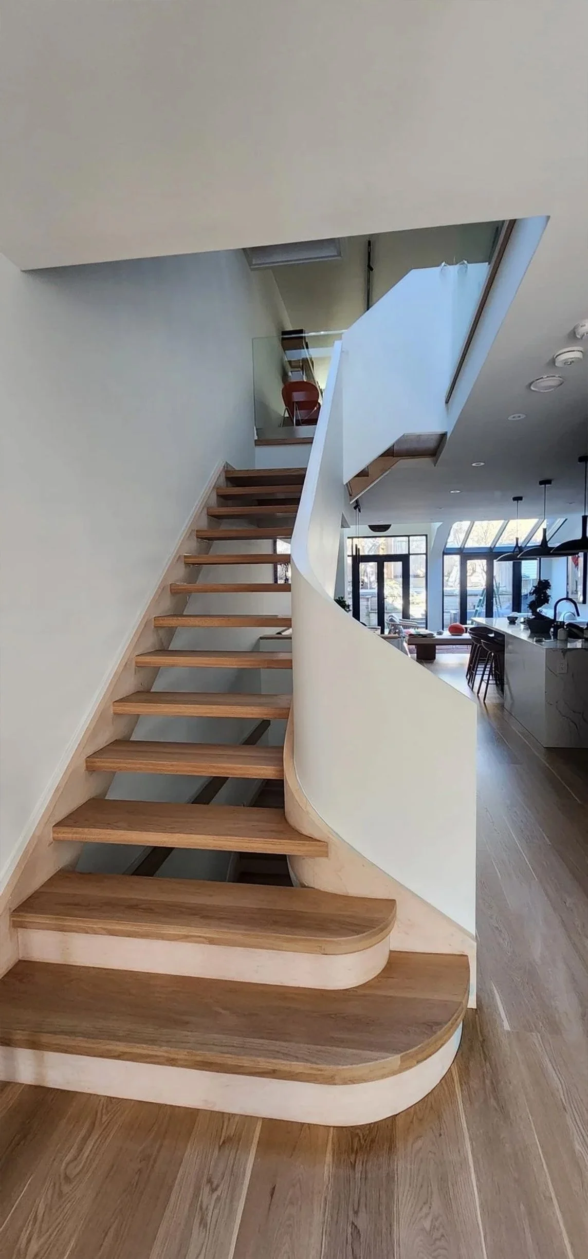 Lantern House staircase in The Beaches, Toronto, built by Maxamin Homes, featuring wooden steps and curved white wall leading to upper floor.