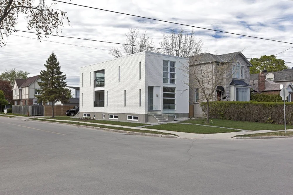 Patio House, a modern white brick custom home in North York, Toronto, built by Maxamin Homes, with balconies, large windows, trees, and sidewalk under cloudy sky.