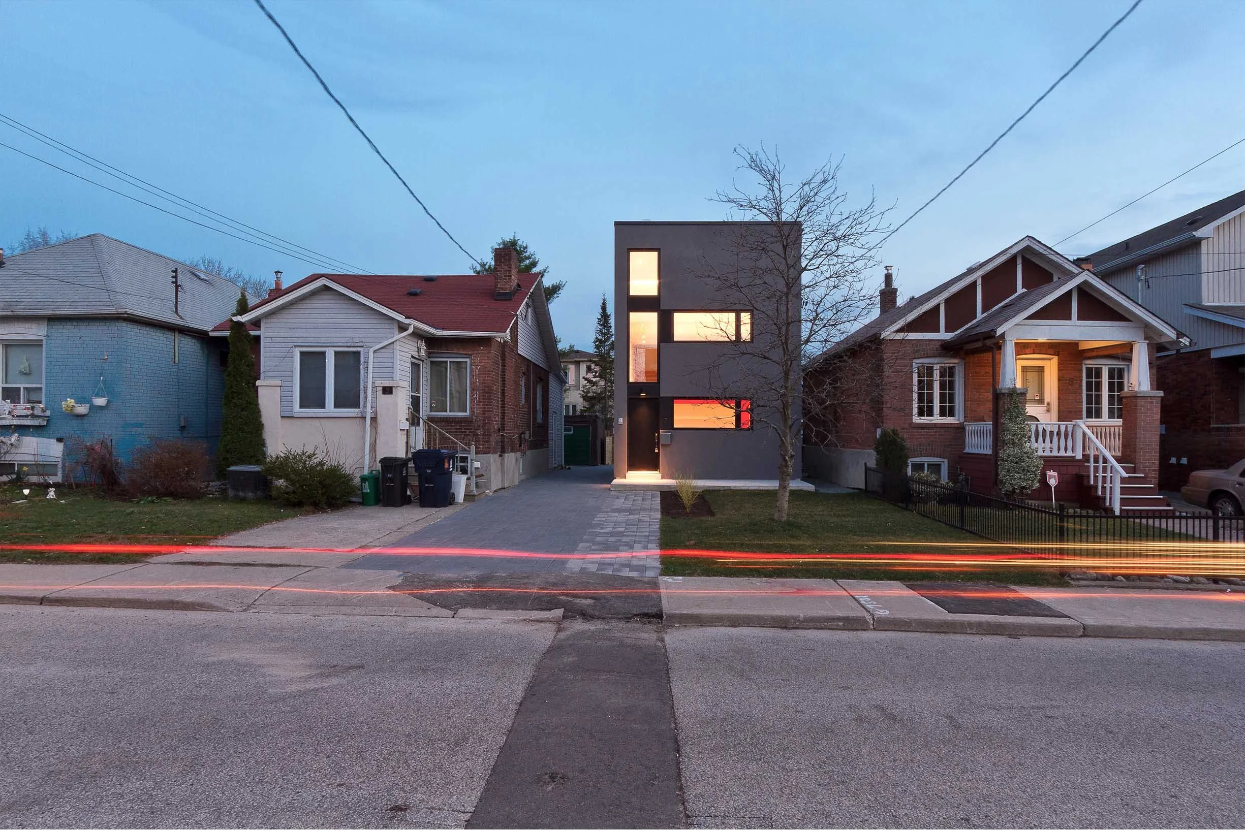 Whale House, a modern gray custom home in East York, Toronto, built by Maxamin Homes, with large windows and light trails from passing cars at dusk.