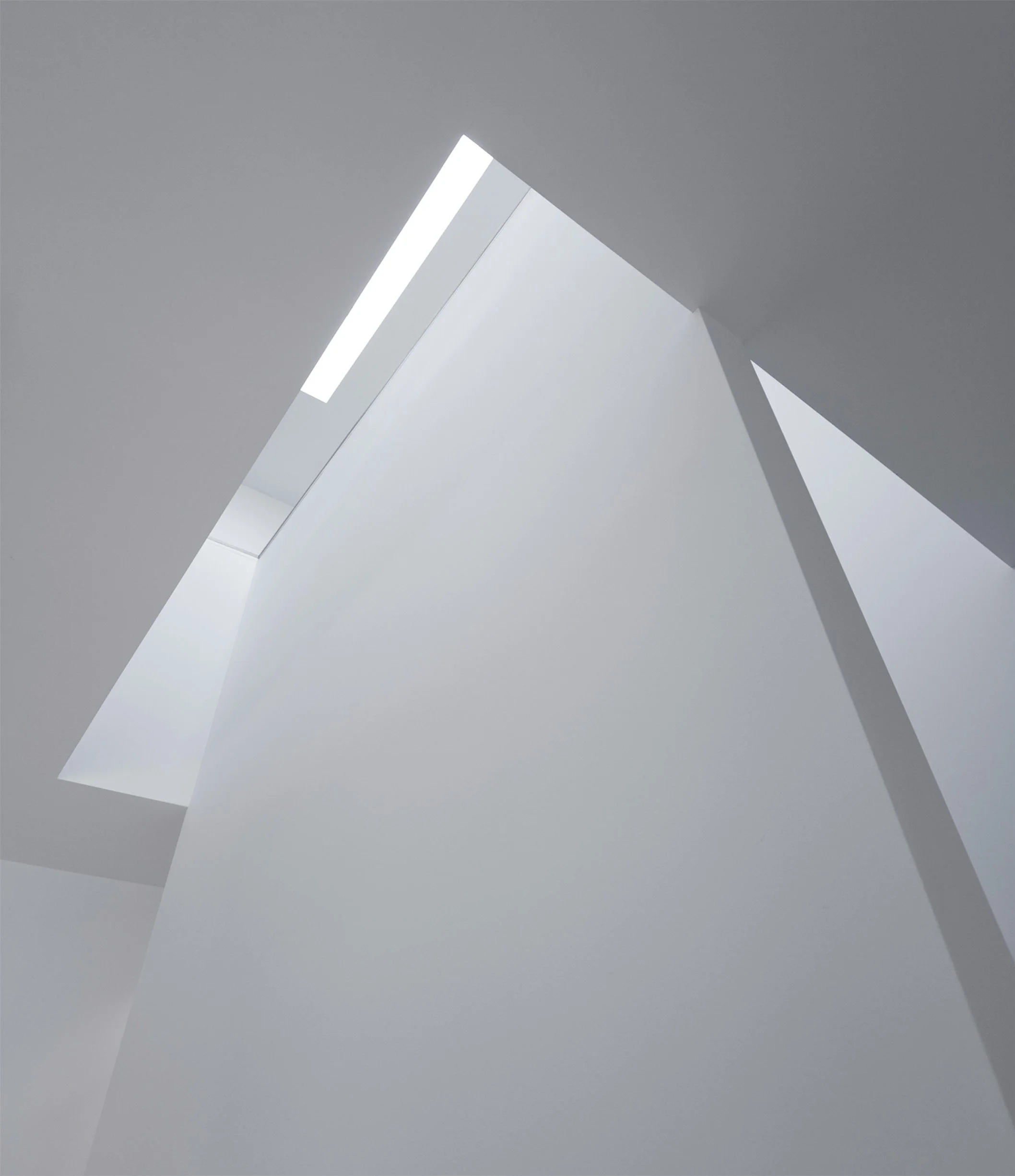 View of a modern interior ceiling with angular design and a long rectangular skylight, illuminated with natural light.