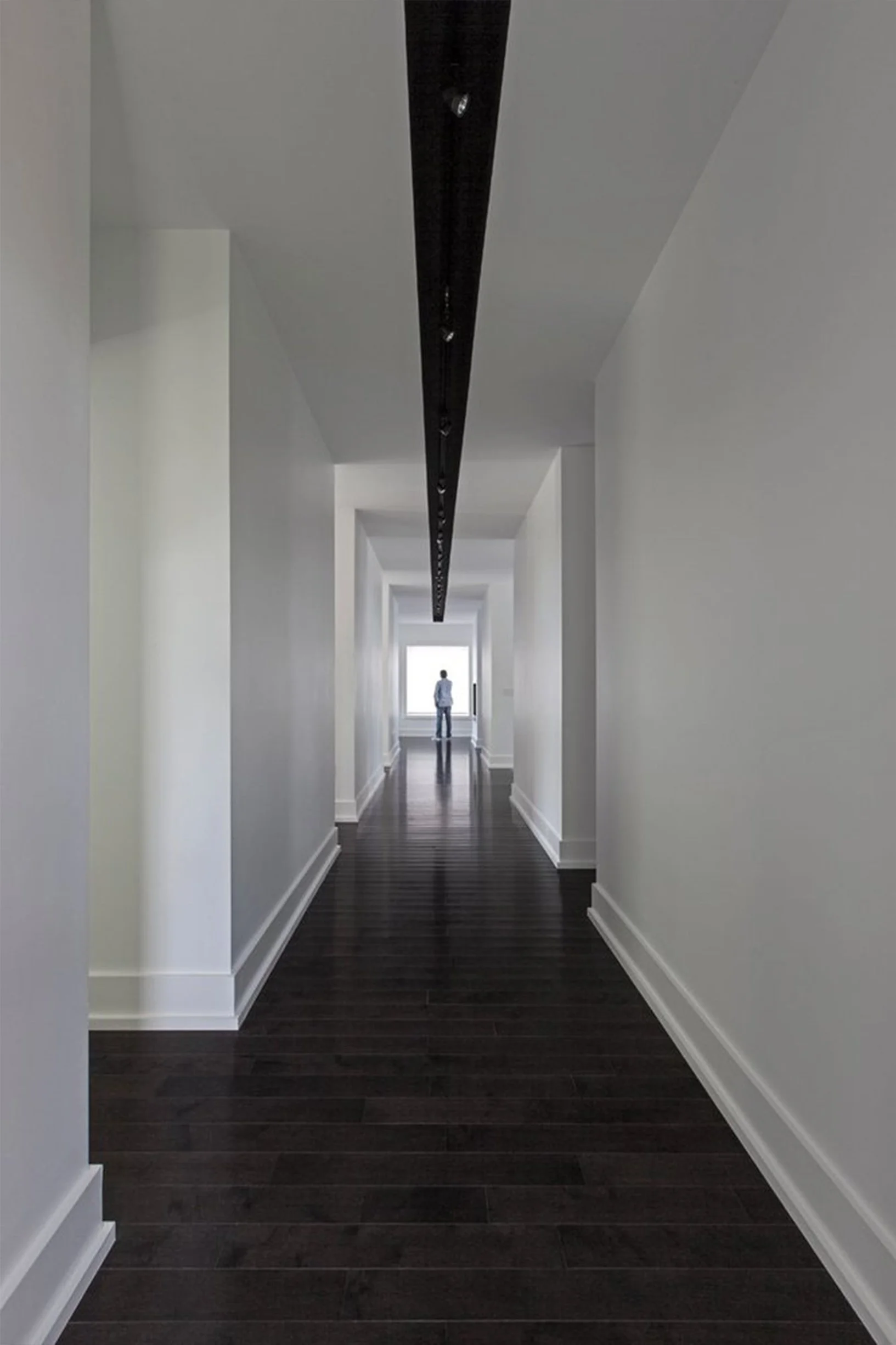 Gallery House hallway in East York, Toronto, built by Maxamin Homes, with white walls, dark wood flooring, track lighting, and window at corridor end.