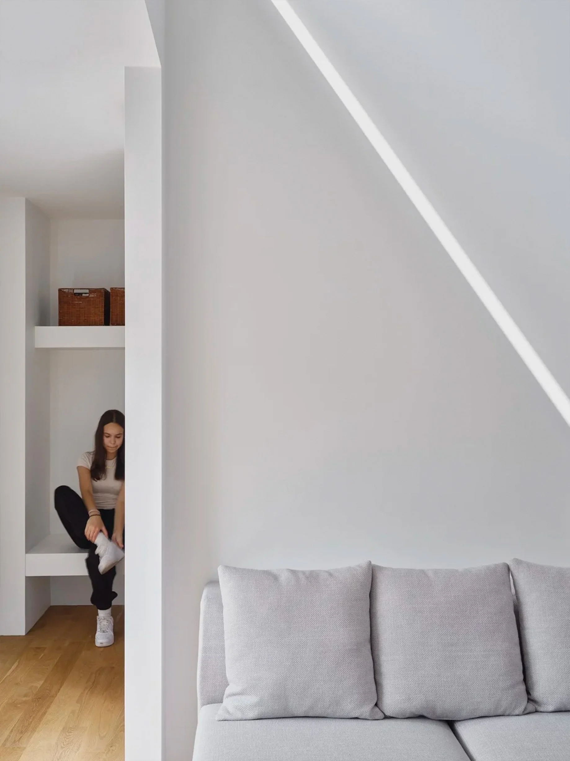 Periscope House interior in East York, Toronto, built by Maxamin Homes, showing a woman tying sneakers on a built-in shelf beside a gray sofa.
